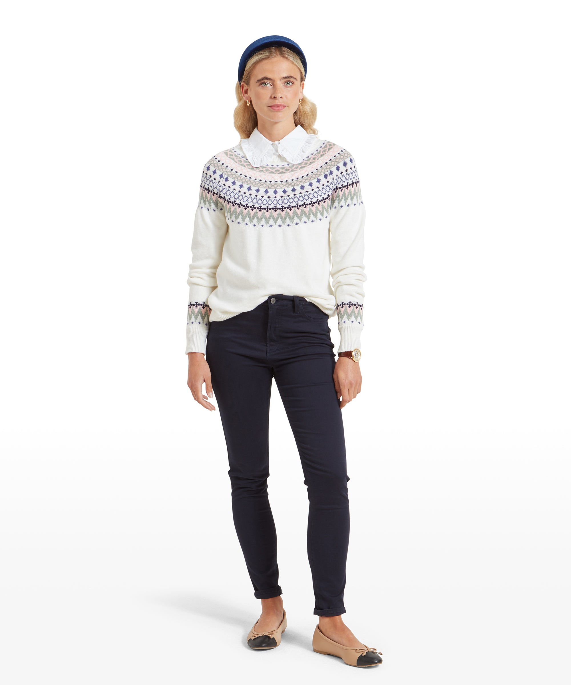 The woman poses in a full-body shot, showing her complete outfit, including the Schöffel Shetland Fairisle Jumper for Women in Pink Blue, dark navy pants, and beige flats. Her look is both comfortable and elegant, ideal for a casual day out or a cosy evening indoors.