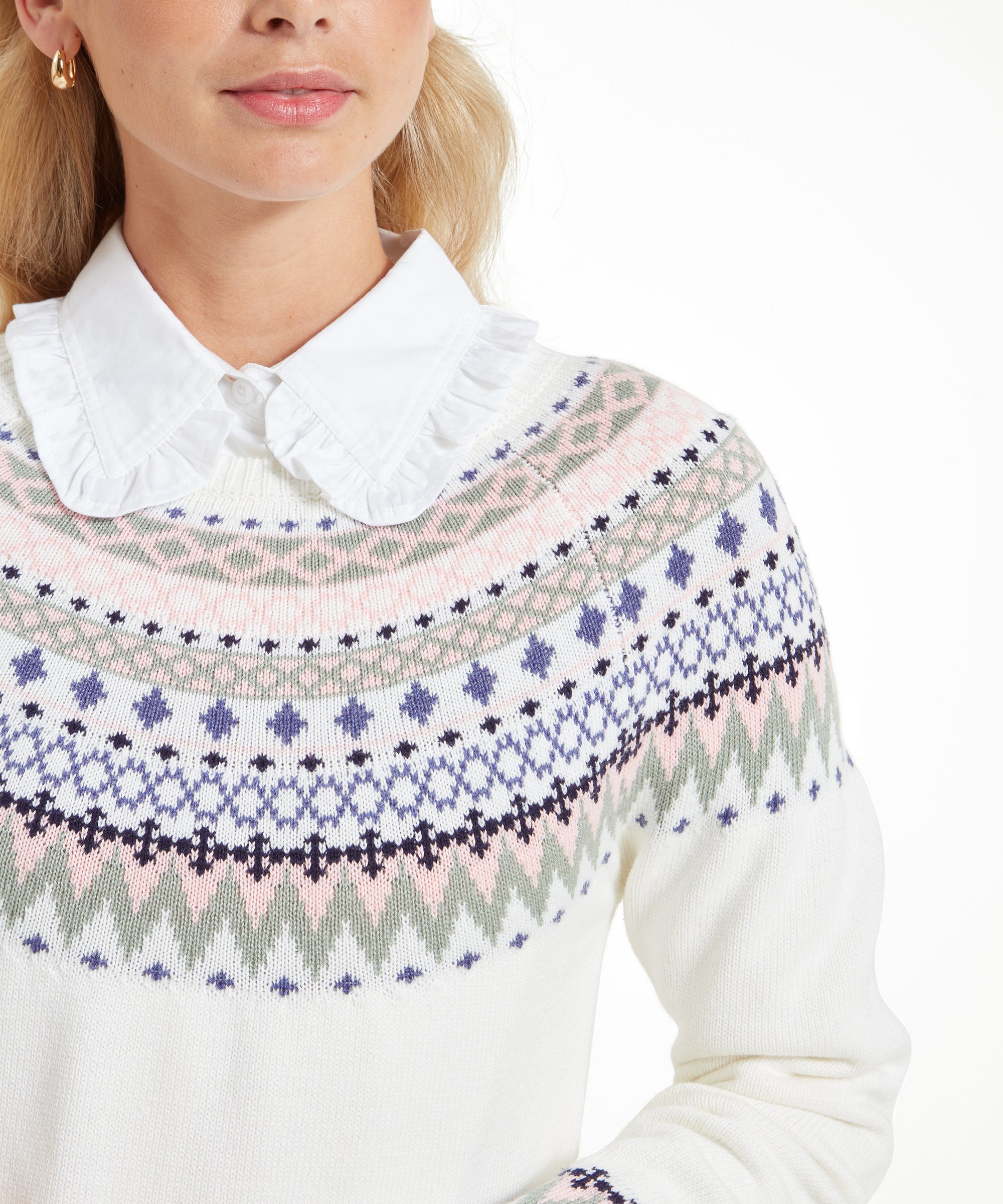 A close-up image focuses on the neckline of the Schöffel Shetland Fairisle Jumper for Women in Pink Blue, displaying the detailed Fair Isle pattern across the chest. The texture of the knit is visible, with the intricate pattern adding a touch of traditional charm to the modern outfit. The woman wears a white collared shirt beneath the sweater, enhancing the classic style.