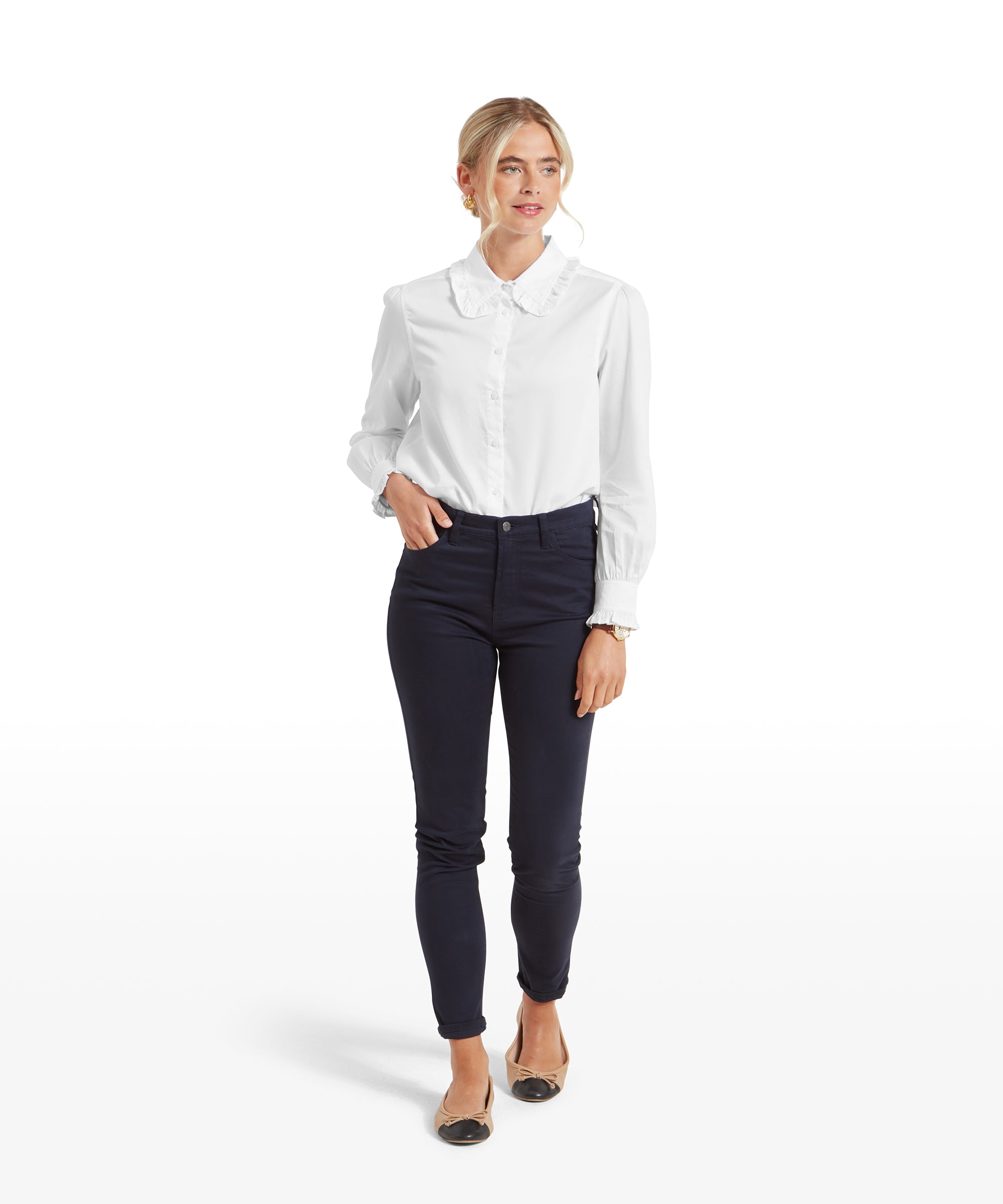 The same woman is shown in a full-body view, wearing the Schöffel Somerleyton Shirt for Women in White and navy pants. She has paired the outfit with nude flats that have a black cap toe. She stands confidently with her arms relaxed by her sides.