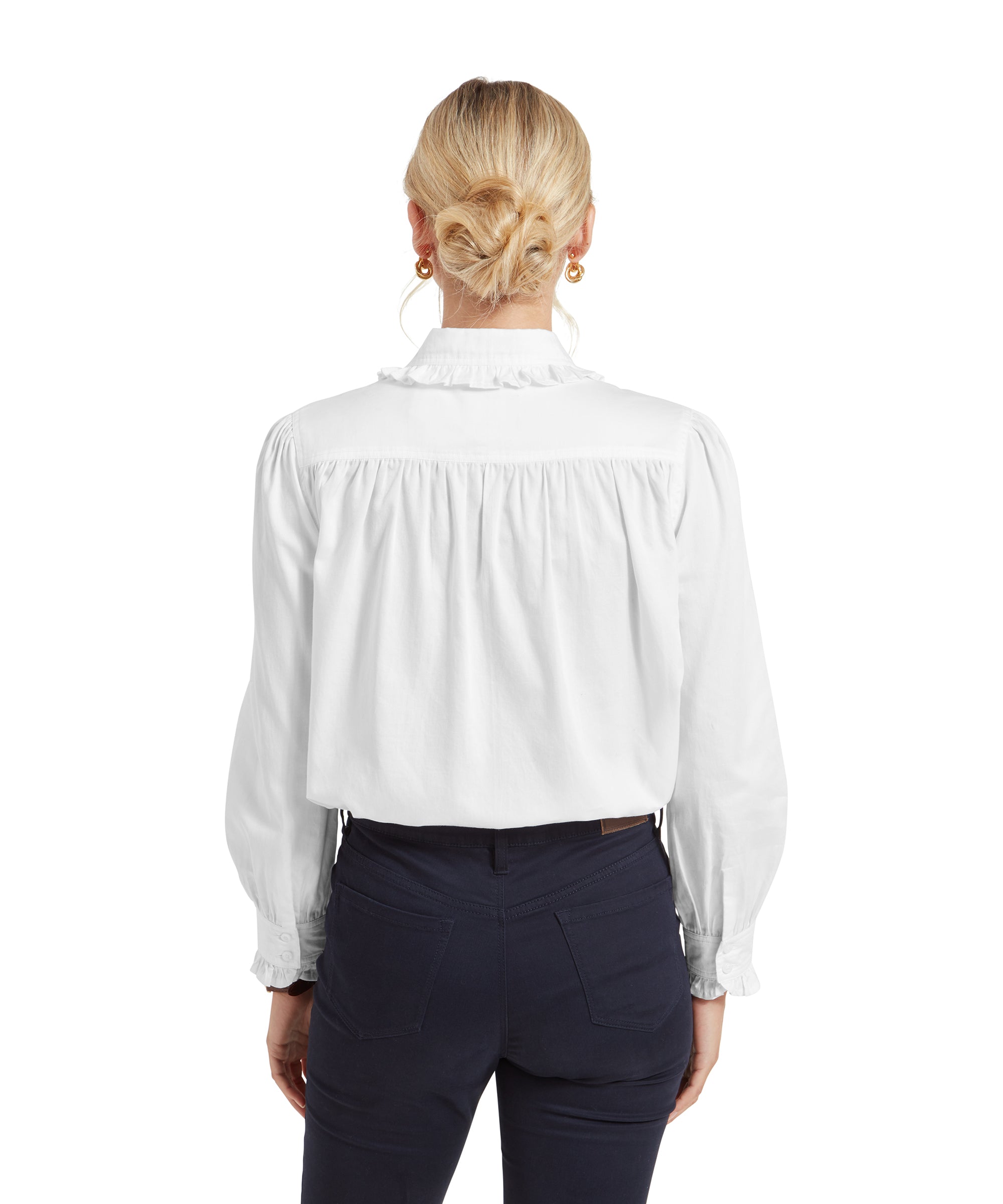 The back of the Schöffel Somerleyton Shirt for Women in White is displayed, showing the gathered detail at the shoulders and the loose, flowing fit of the fabric. The woman’s blonde hair is tied up in a neat bun.