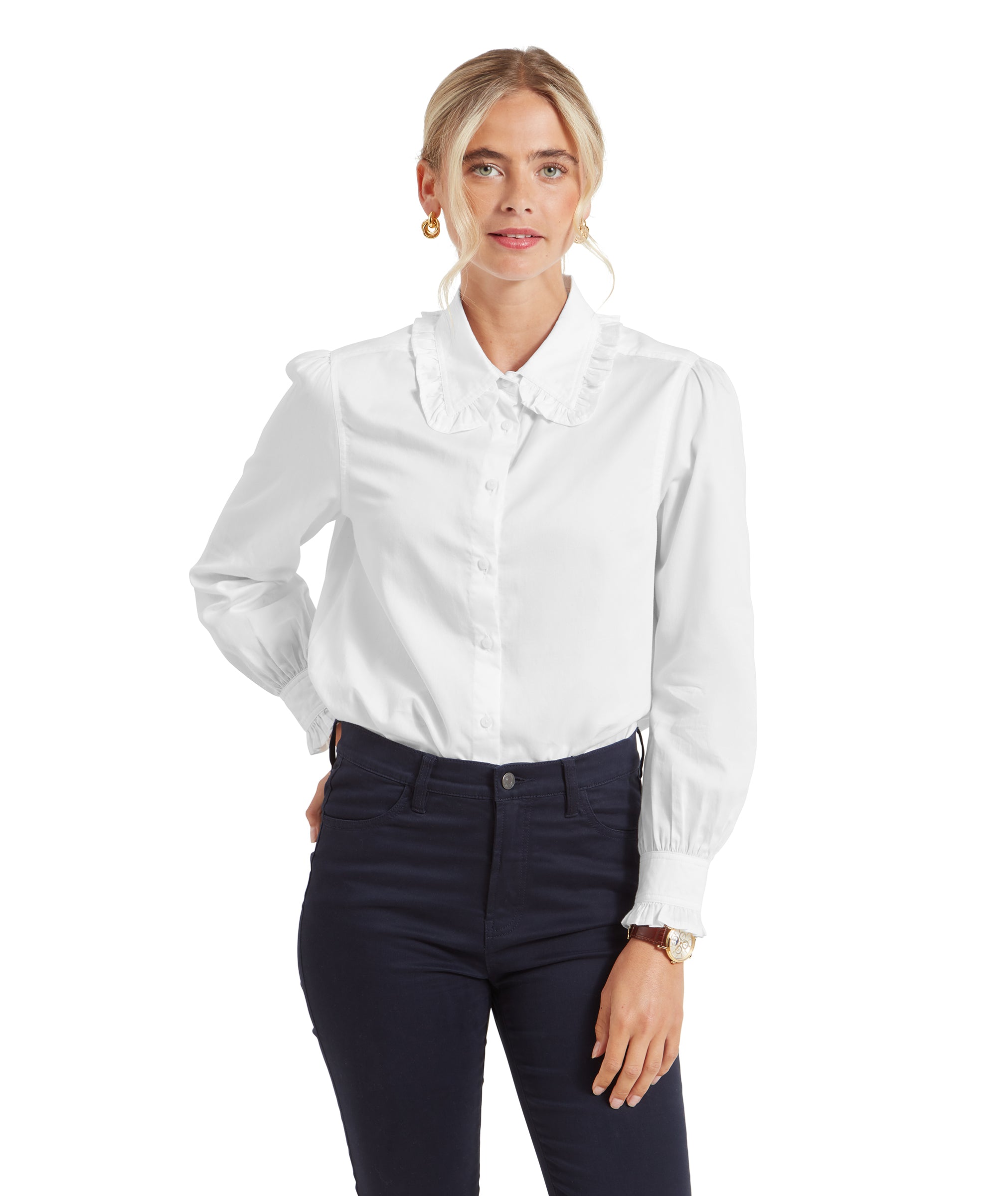 The woman poses with one hand resting on her hip, showing the front of the Schöffel Somerleyton Shirt for Women in White more clearly. The ruffled collar and the puffed sleeves are well defined, emphasising the elegant design.