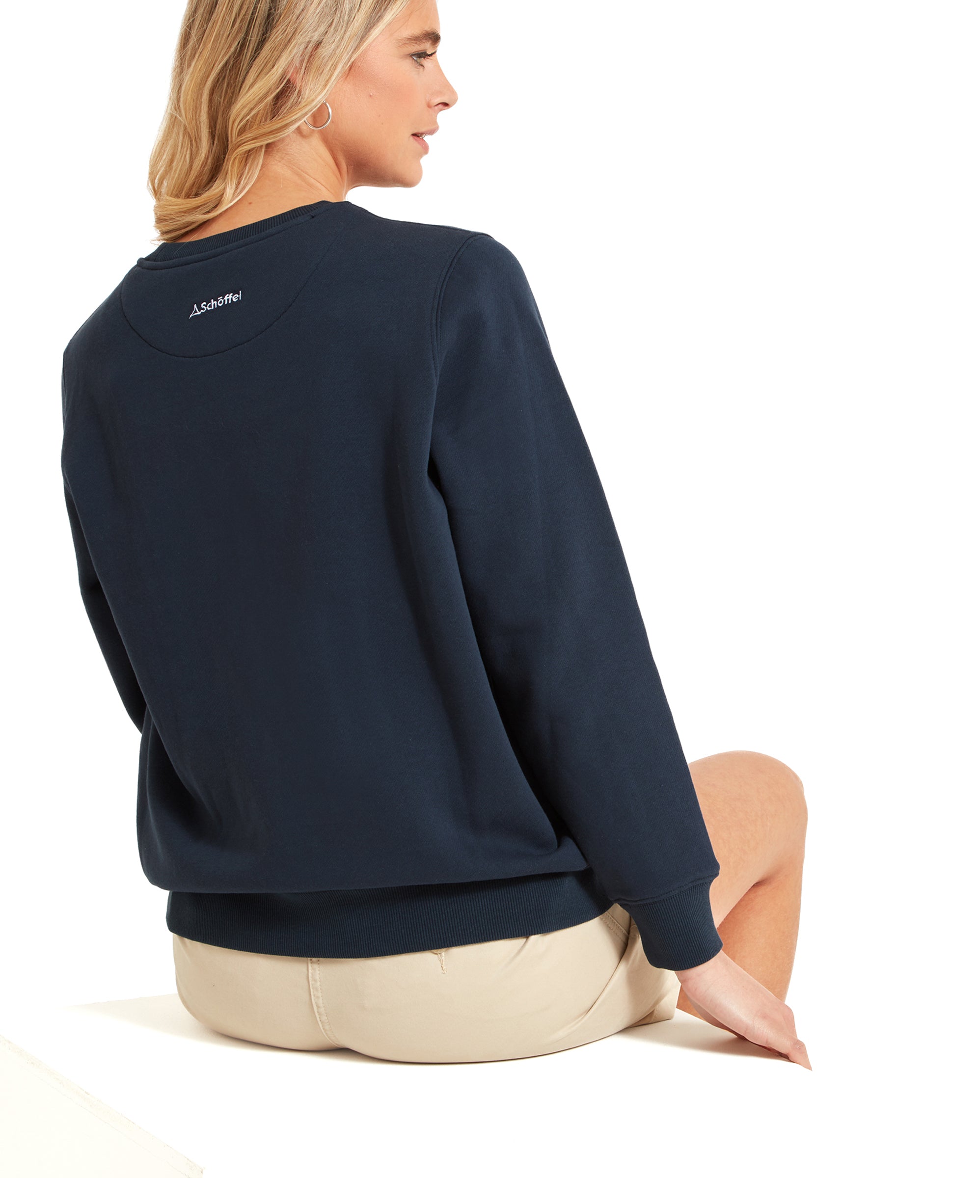 The back view of the woman wearing the Schöffel St Helier Sweatshirt for Women in Navy. She is sitting, showing the back of the sweatshirt and the beige shorts she is wearing.