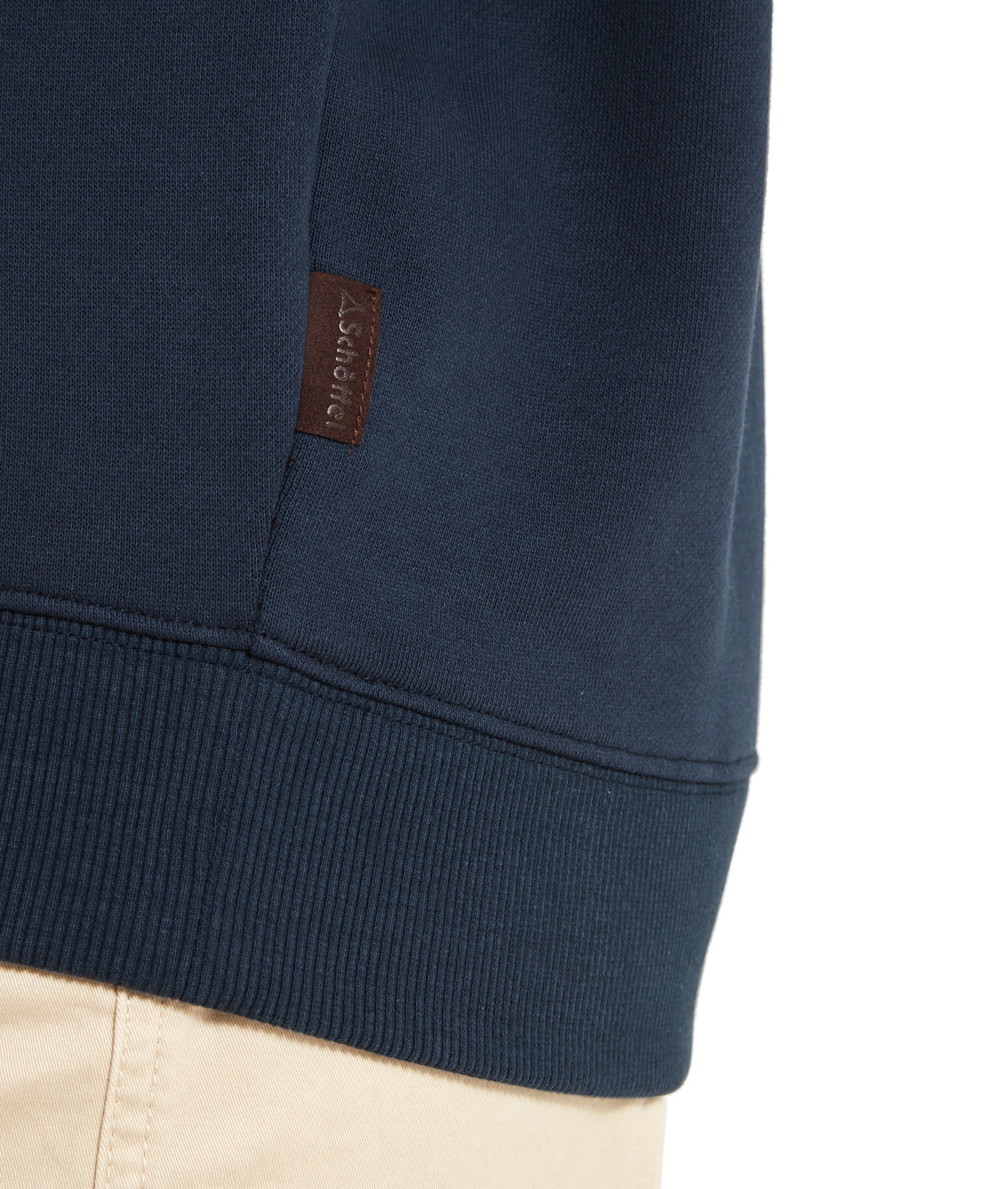 A close-up of the Schöffel St Helier Sweatshirt for Women in Navy, focusing on the ribbed hem and a small brown leather tag with the Schöffel logo, along with a part of her beige shorts.