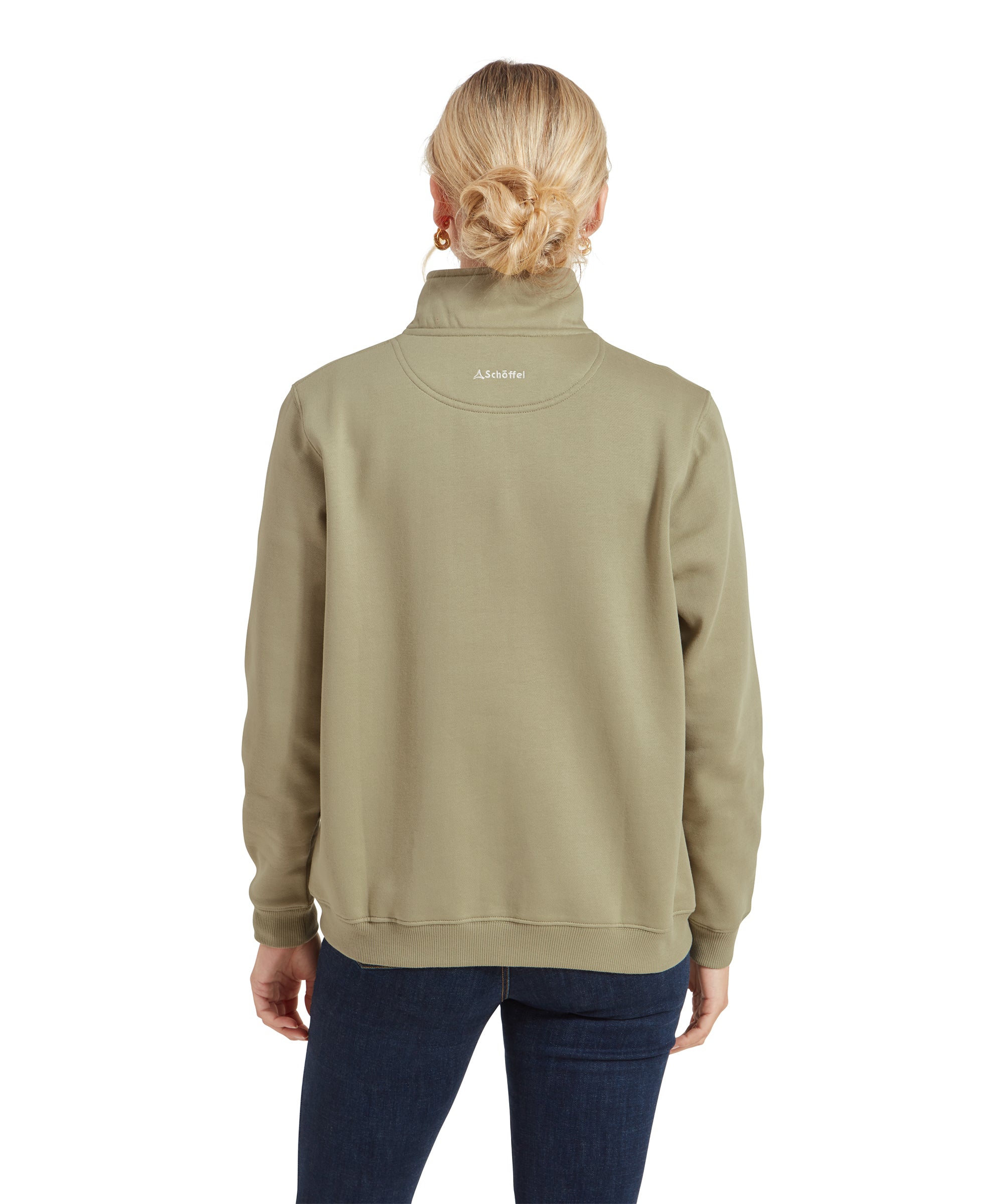 A back view of the model, showing the rear details of the Schöffel St Issey Sweatshirt for Womens in Green. The back of the sweatshirt features a small Schöffel logo embroidered just below the collar. Her hair is styled in a loose, low bun, and she is wearing dark skinny jeans.