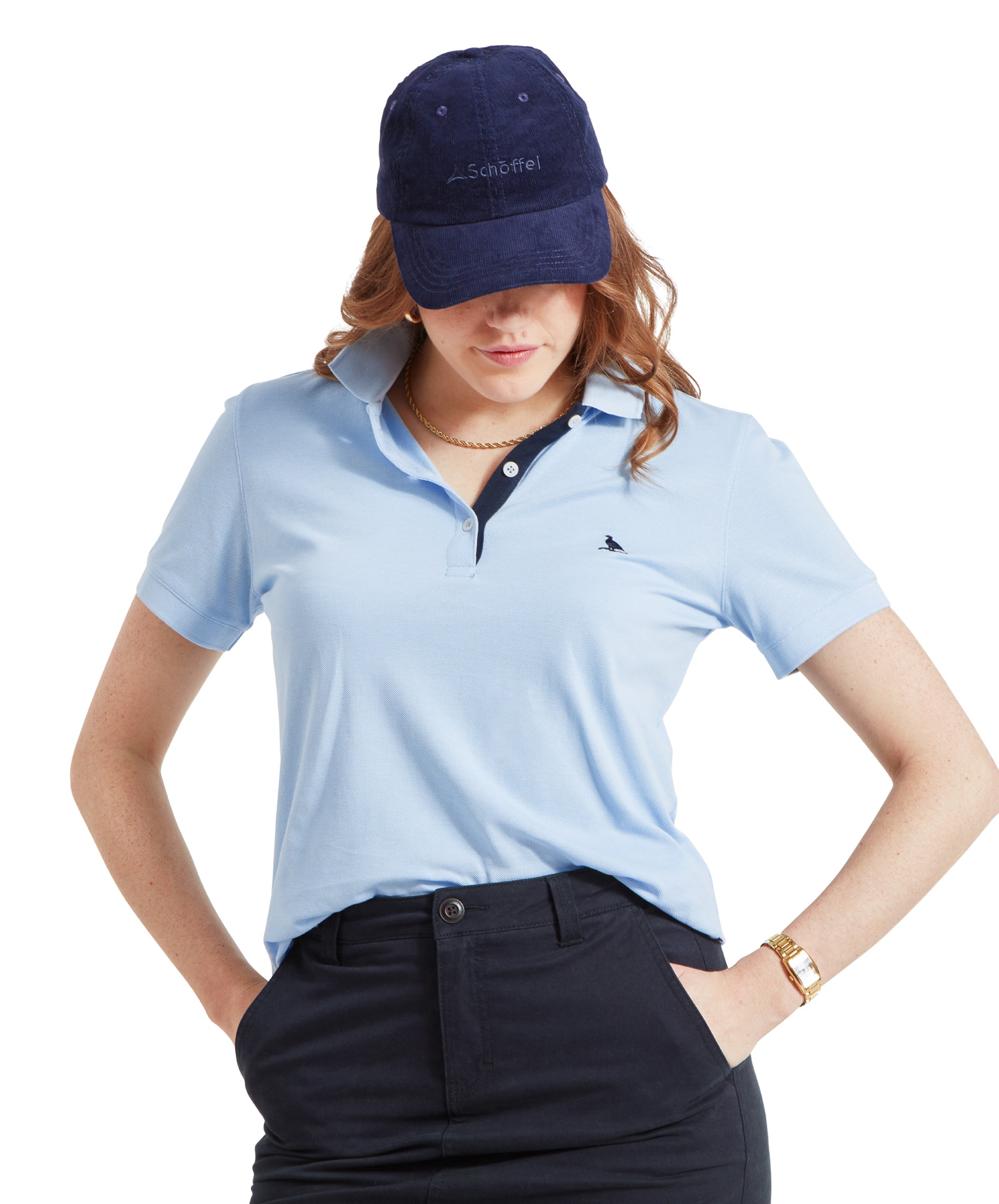 A woman wearing a Schöffel Women's St Ives Polo Shirt for Women in Blue with a navy cap, standing with her hands in her pockets.