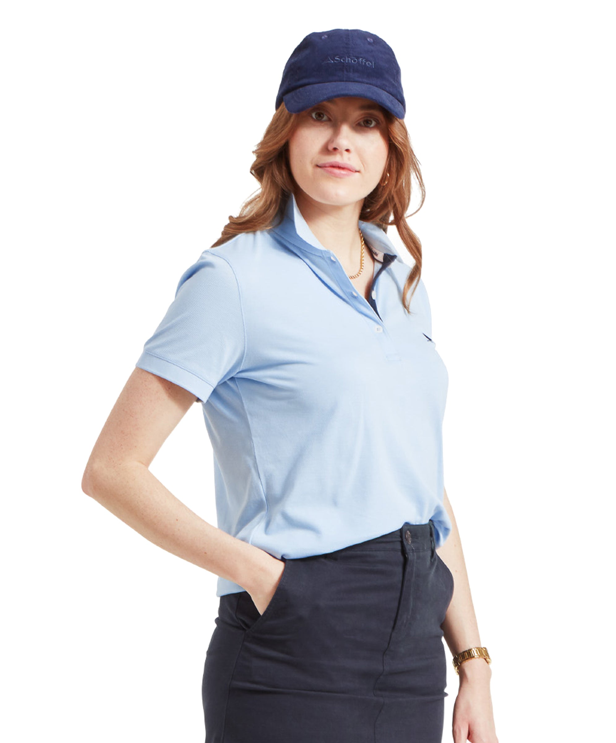 A side view of a woman in a Schöffel Women's St Ives Polo Shirt for Women in Blue and navy skirt, wearing a navy cap and smiling slightly.