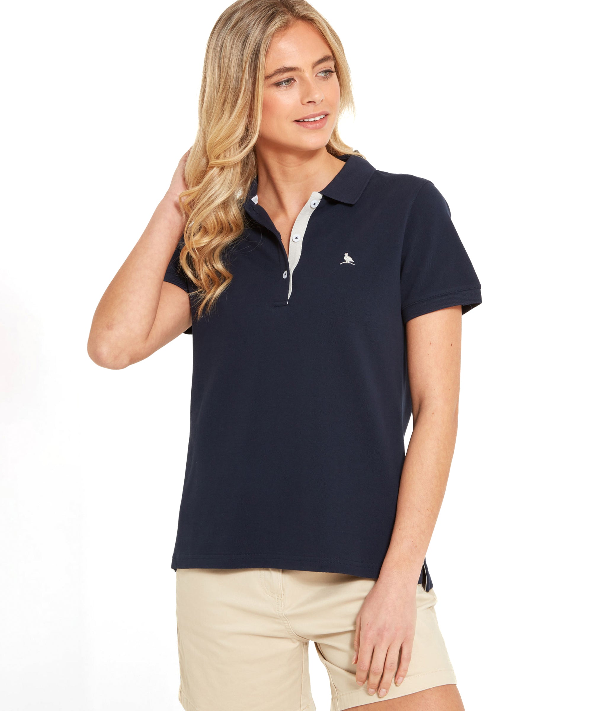 A woman wearing a Schöffel Women's St Ives Polo Shirt for Women in Navy and beige shorts, posing with one hand in her hair.