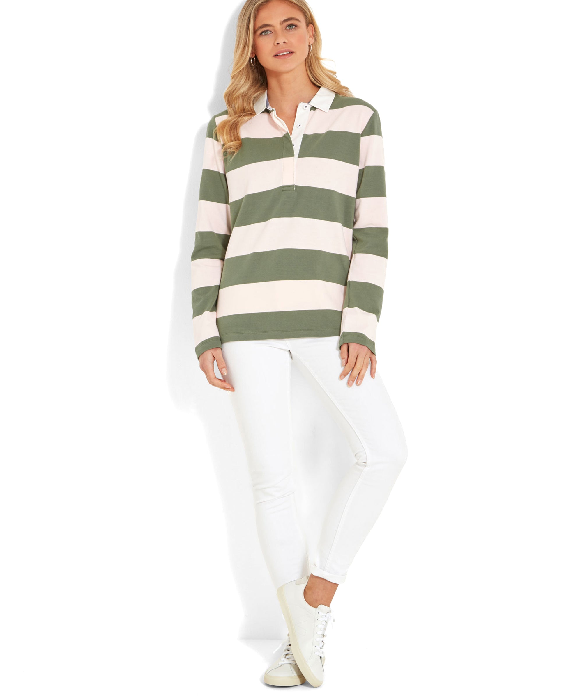 A full-body shot of the woman wearing the Schöffel St Mawgan Rugby Shirt for Women in Pink and olive green striped. She stands against a white background with her hands by her sides. The outfit is completed with white slim-fit jeans and white trainers.