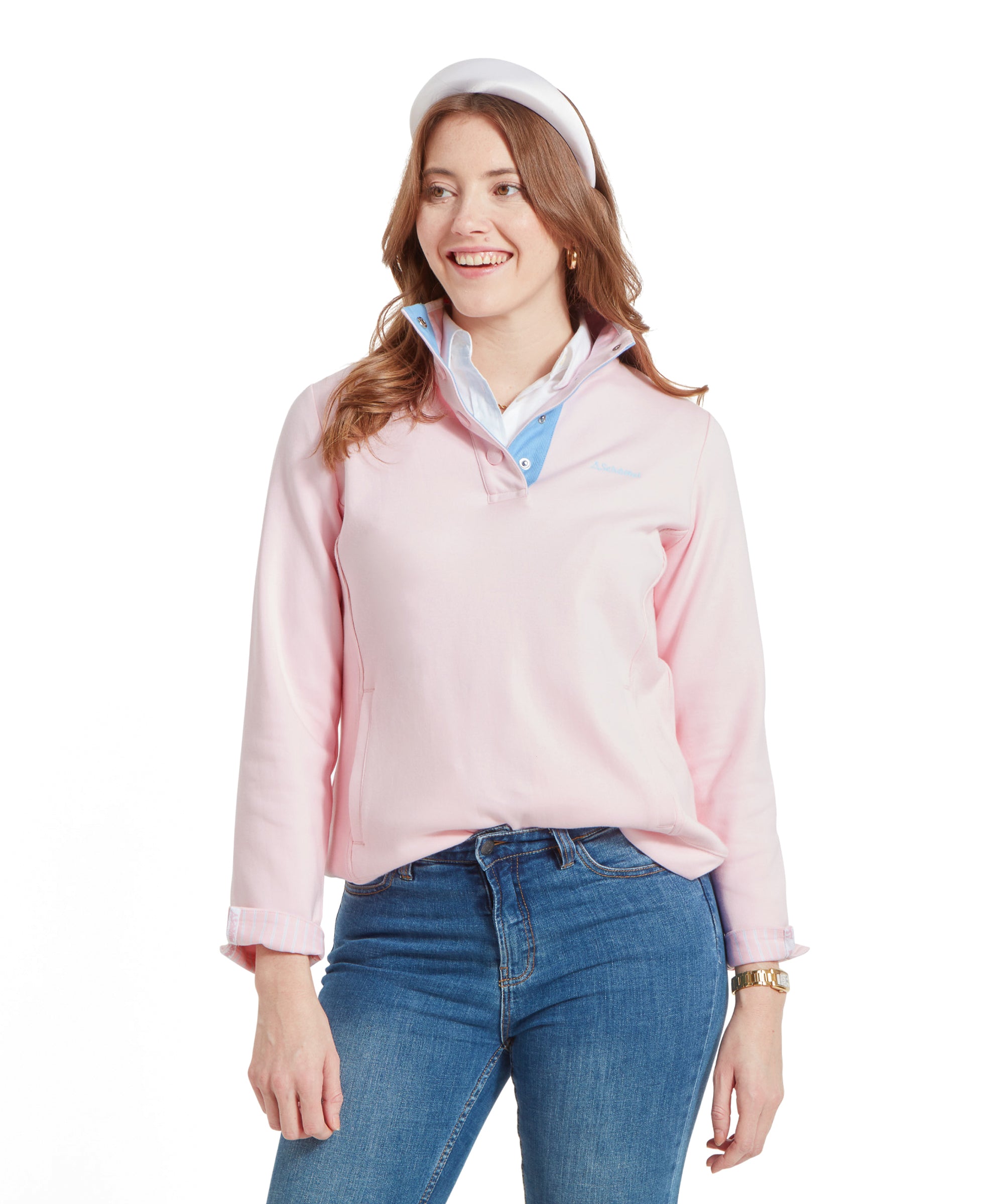 A woman is wearing a Schöffel Steephill Cove Sweatshirt for Women in Pink, layered over a white collared shirt, paired with blue jeans. She is smiling and looking to the side, with her left hand casually placed in the front pocket of the sweatshirt.