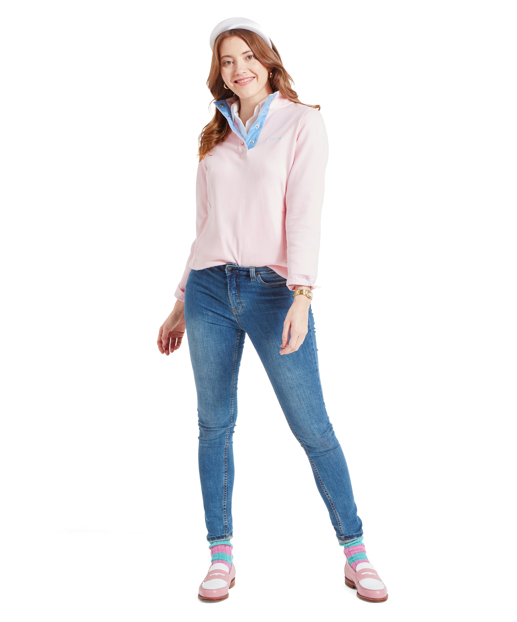 Full-body image of the woman in the Schöffel Steephill Cove Sweatshirt for Women in Pink, white collared shirt, and blue jeans. She is standing and smiling, wearing a white headband and pink shoes with blue and pink striped socks.