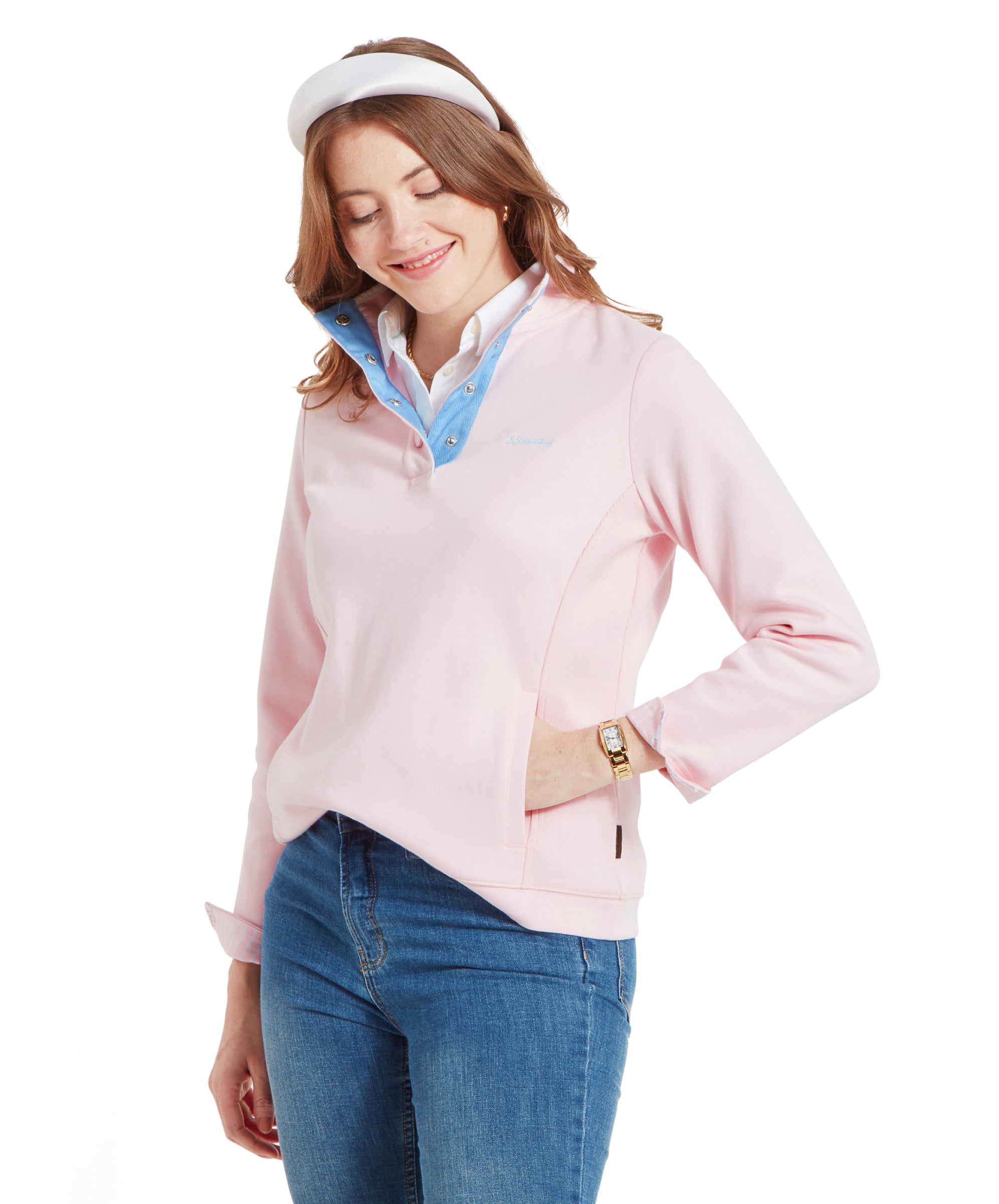 The woman is posing with her hands in the front pockets of her Schöffel Steephill Cove Sweatshirt for Women in Pink. She is looking down and smiling, showing off the light blue inner collar of the sweatshirt.