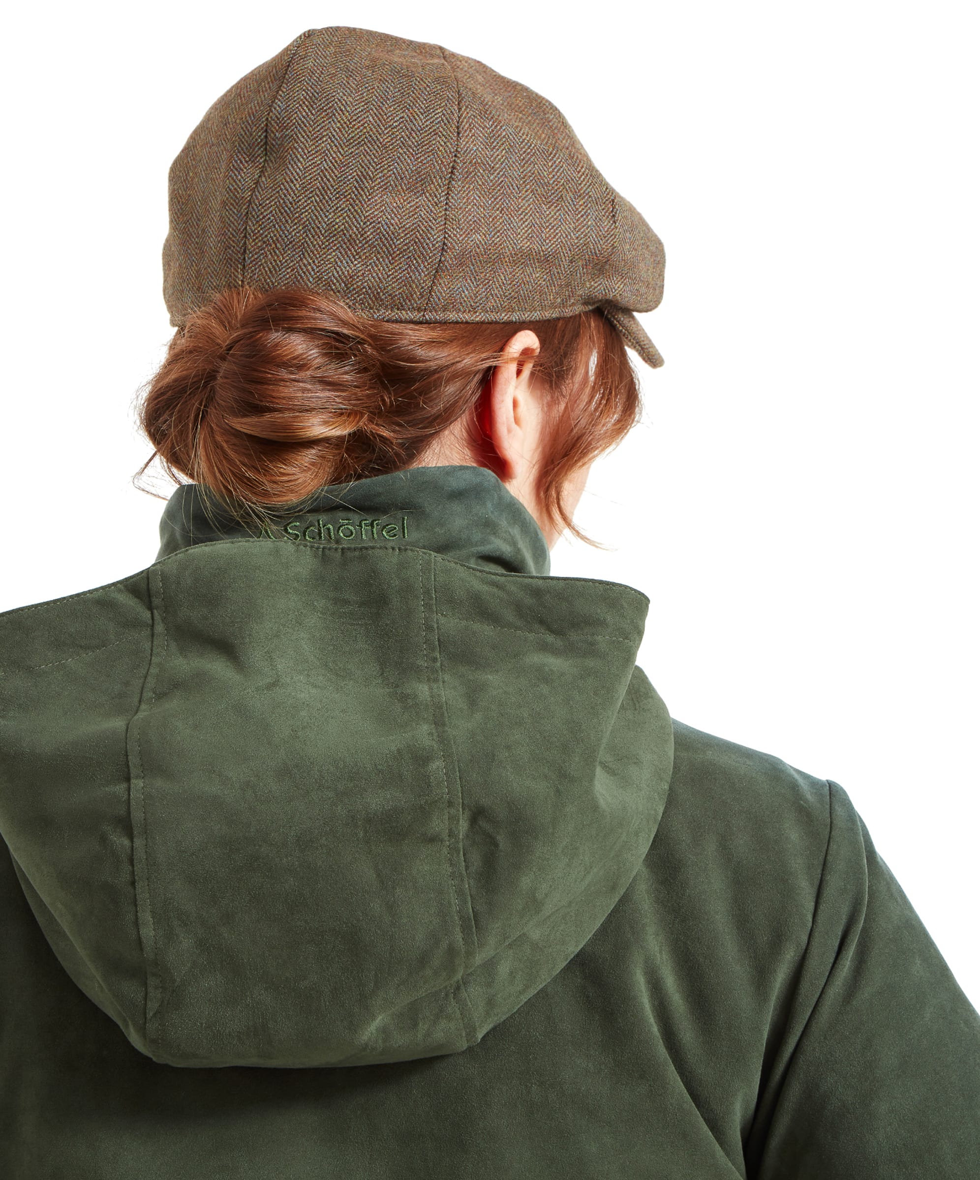 A rear shot of the Schöffel Teal Shooting Coat for Women in Green with its hood attached, covering the back of the collar. The jacket has a deep green suede-like texture. The woman’s hair is tied up under the tweed flat cap, and the collar still displays the “Schöffel” logo embroidery.