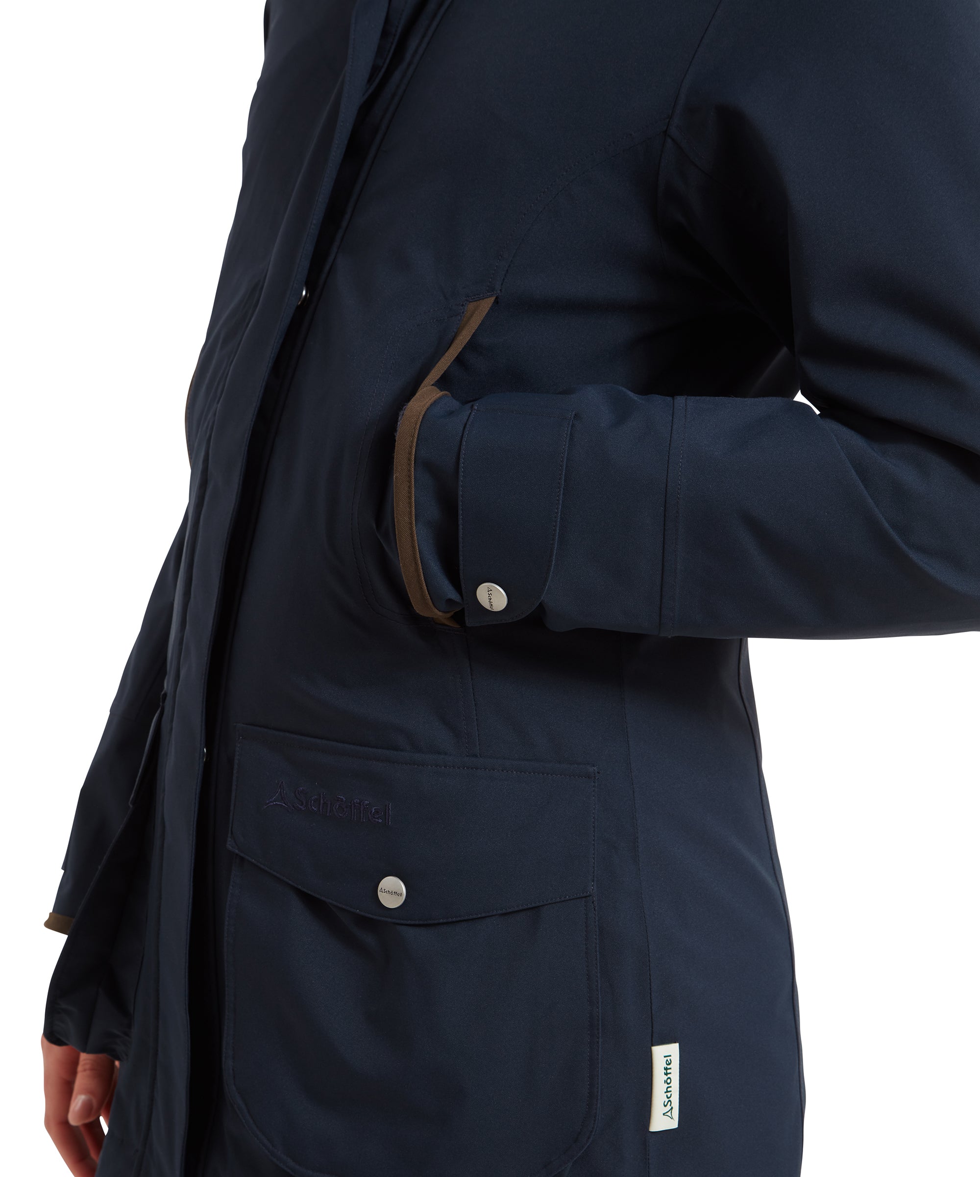 A close-up shot of the side of the Schöffel Teal Ultralight Coat for Women in Blue, with the woman’s hand resting in the pocket. The brown trim around the pocket opening and the sleeve cuff detail are highlighted, emphasising the jacket’s functional design and attention to detail.