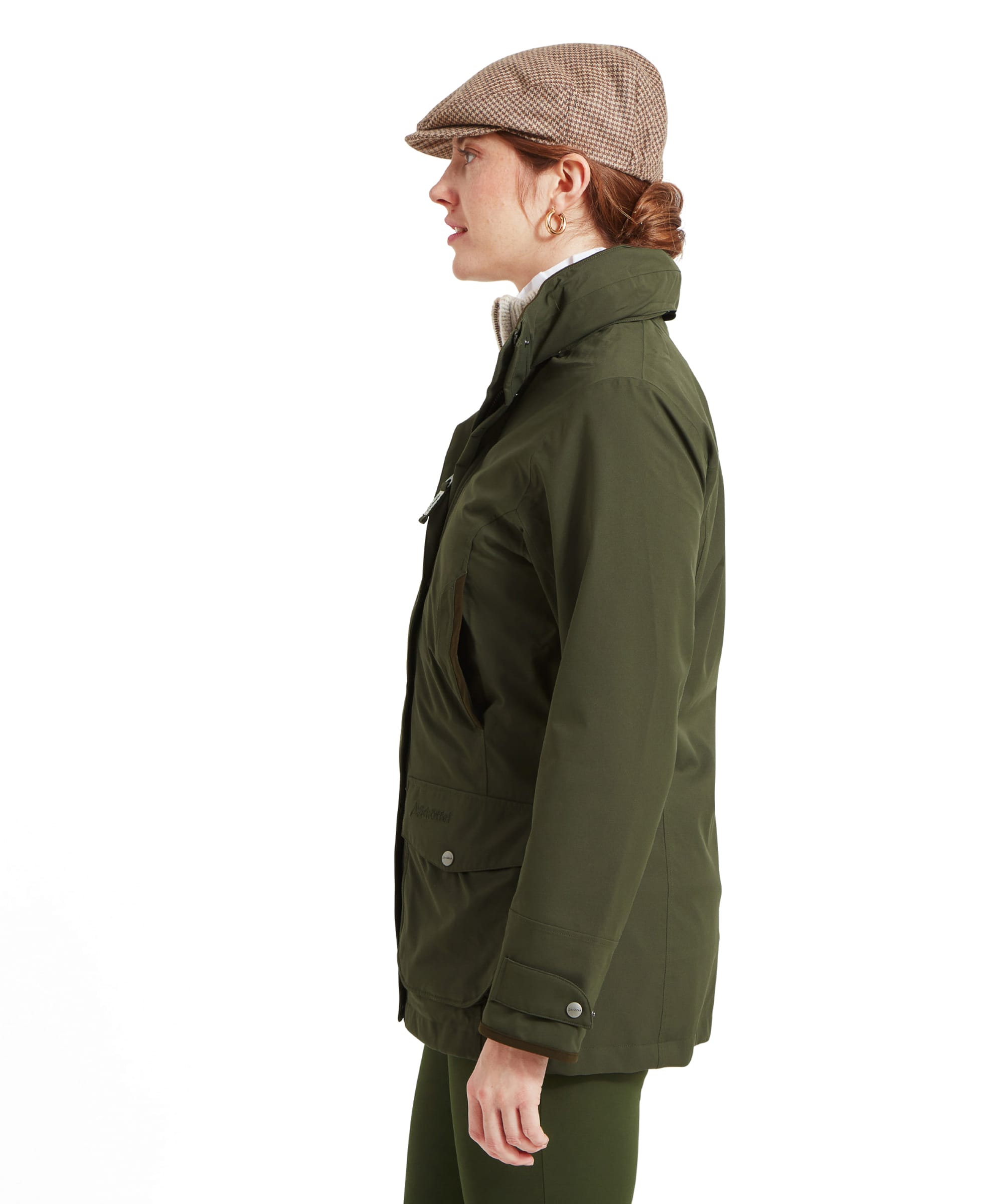 The woman is captured from the side, showing the profile of the Schöffel Teal Ultralight Coat for Women in Green. The jacket has a high collar and a tailored fit, with subtle stitching details. The cap and her hair are visible from the side, emphasising the classic and practical look.