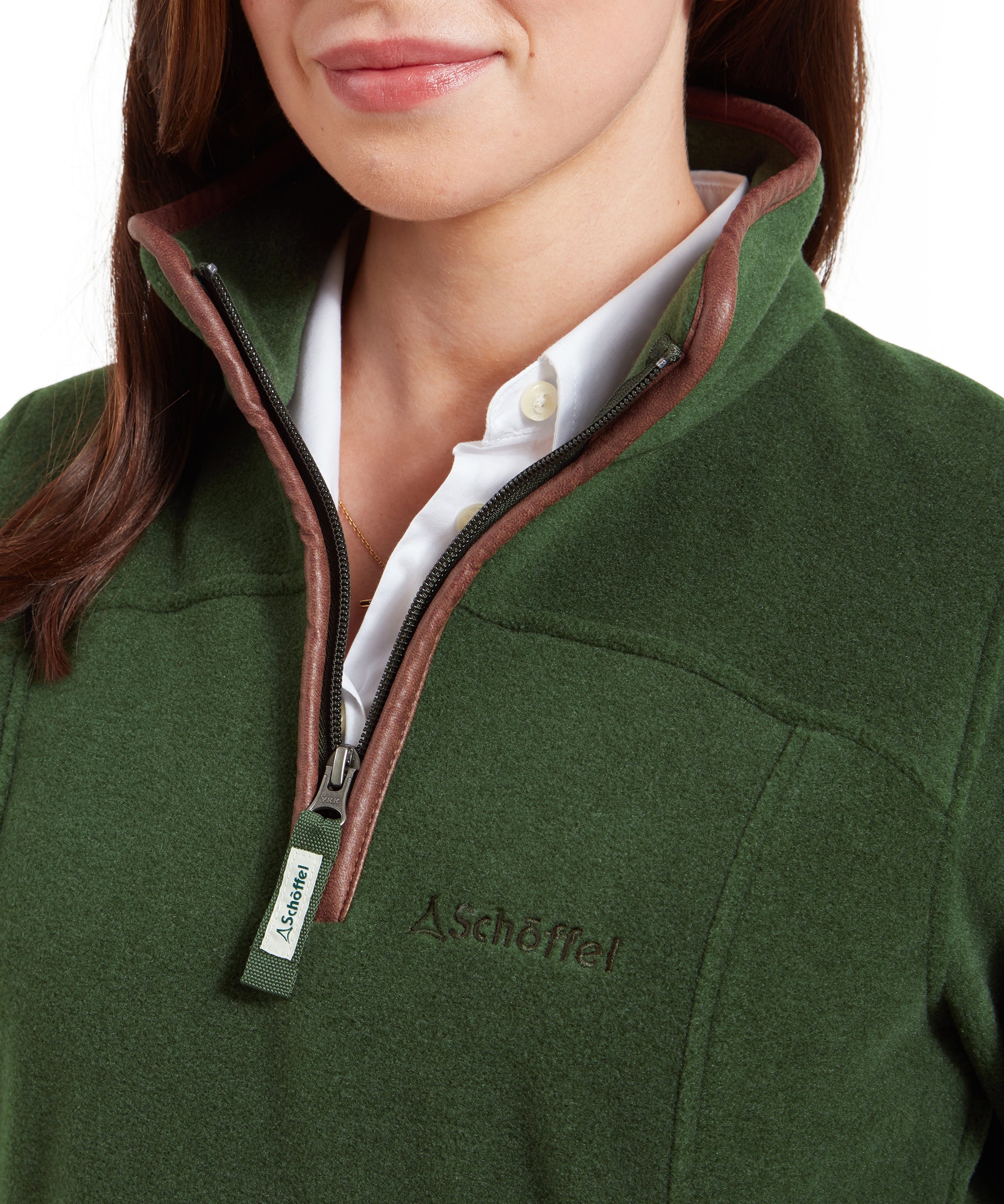 This image focuses on the front of the Schöffel Tilton 1/4 Zip Fleece for Women in Light Green, showing the brown trim around the collar and zipper. The high collar is slightly open, revealing a white button-up shirt underneath. The brand’s logo is embroidered on the chest, and the zipper pull is labeled with the brand name, highlighting the quality and design.