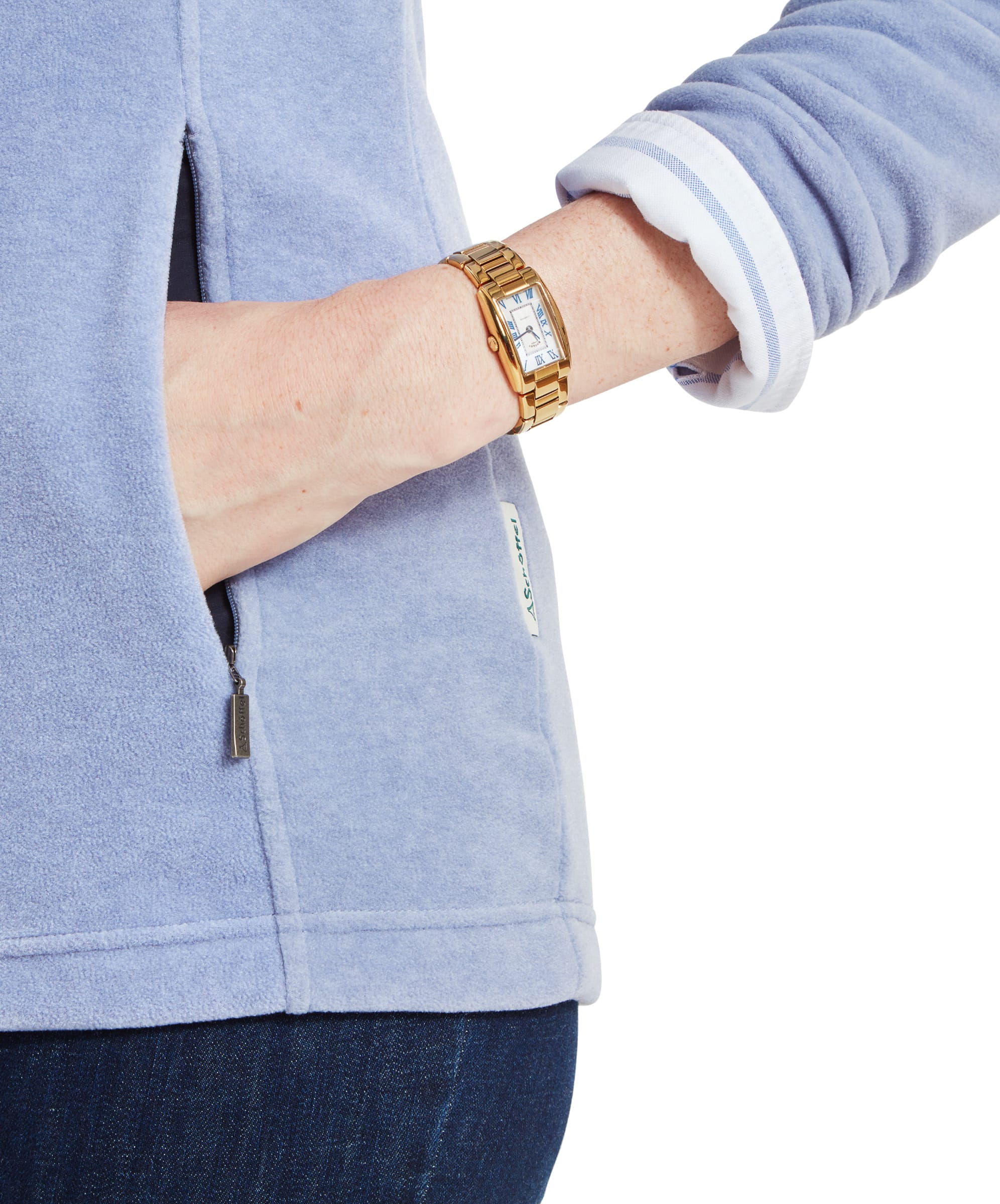 This image focuses on the lower section of the Schöffel Tilton 1/4 Zip Fleece for Women in Light Blue, showing the woman’s hand tucked into the pocket. The light blue fabric contrasts with her dark jeans, and a gold wristwatch is visible on her wrist. The zipper pull and logo tag near the pocket are also in view, highlighting the attention to detail in the design.