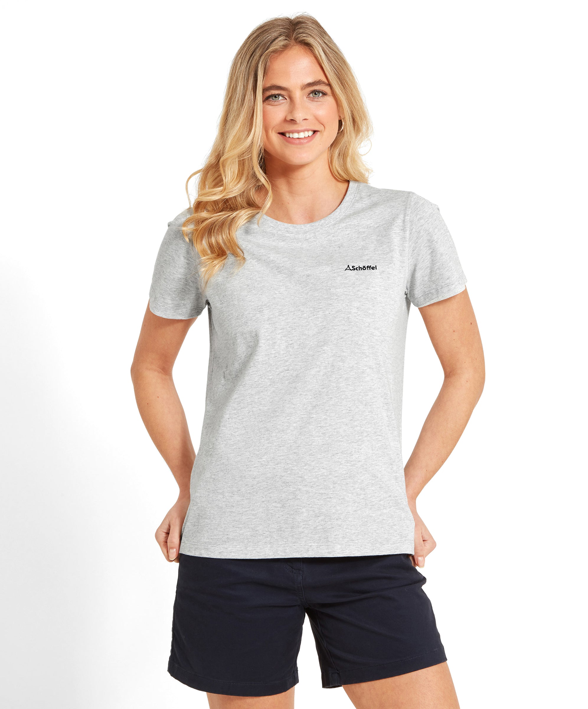 Woman wearing a Schöffel Tresco T Shirt for Women in Grey with "Schöffel" logo, standing with hands in pockets, smiling.