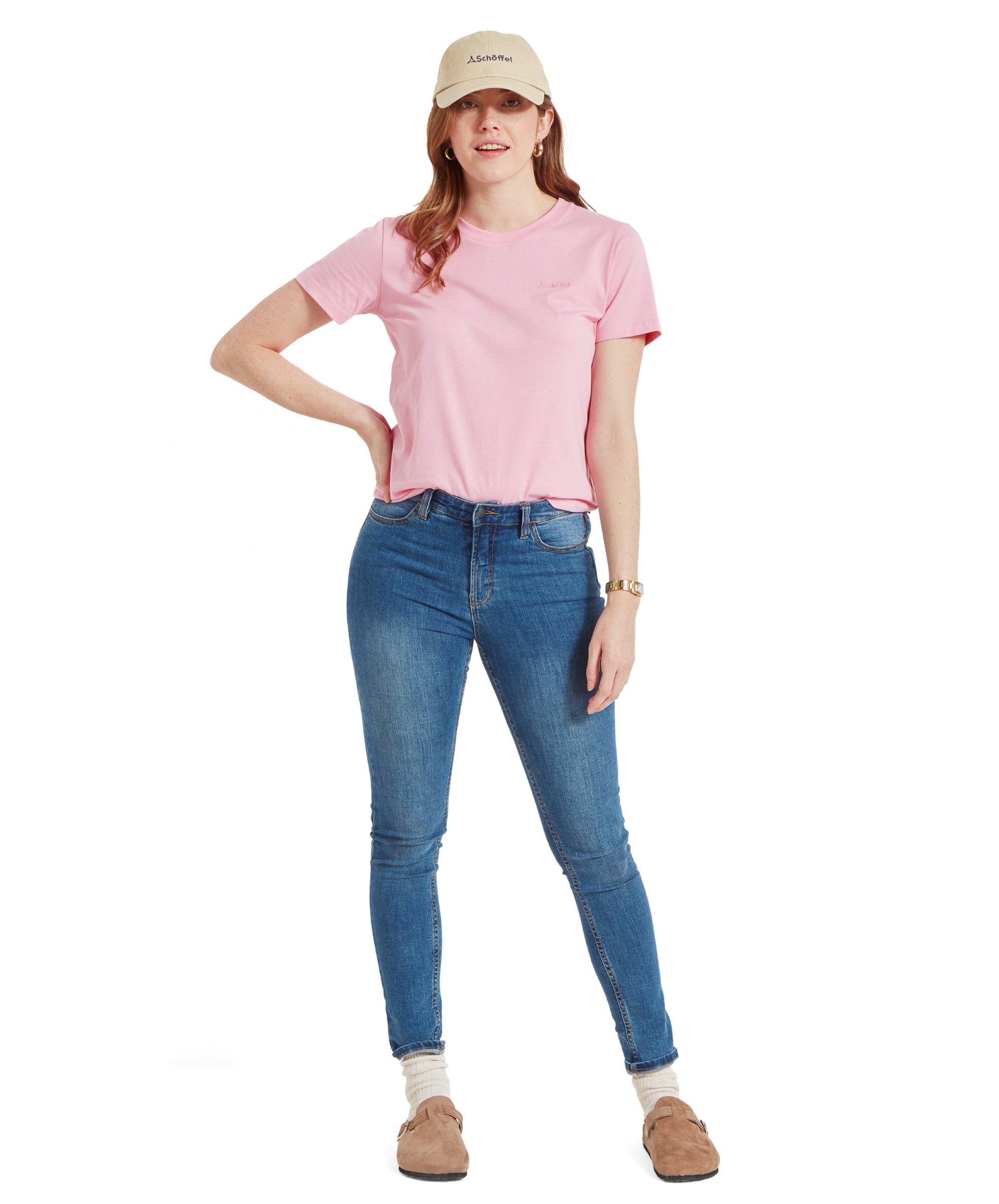 Full-body shot of the model in Schöffel Women's Tresco T-Shirt in Pink, blue jeans, beige cap, standing with a hand on hip.