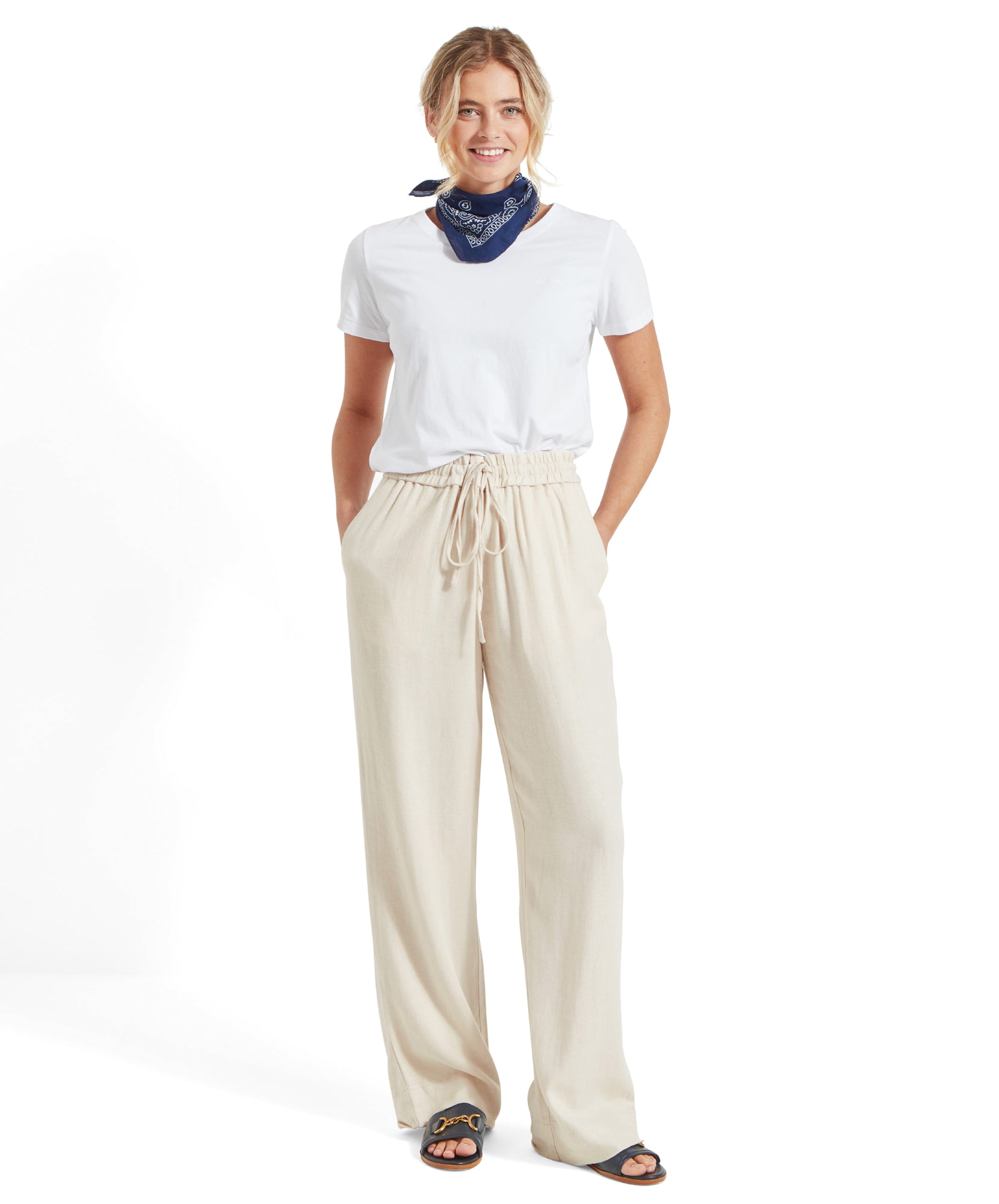 A woman wearing the Schöffel Tresco T Shirt for Women in White, paired with beige wide-leg trousers and a blue bandana, smiling and looking straight ahead.