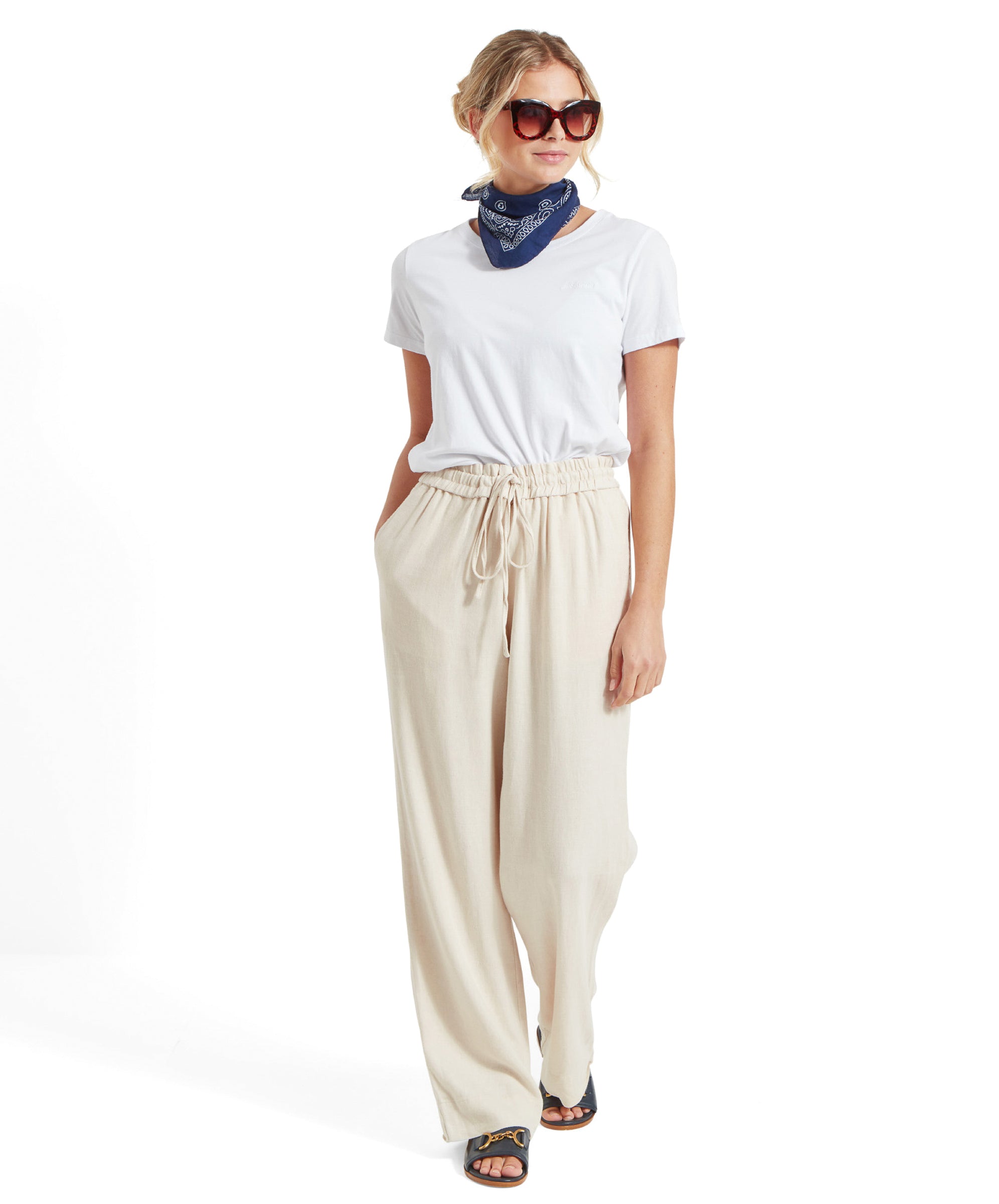 Full-body view of the woman in the Schöffel Tresco T Shirt for Women in White, beige wide-leg trousers, and blue bandana, walking and smiling.