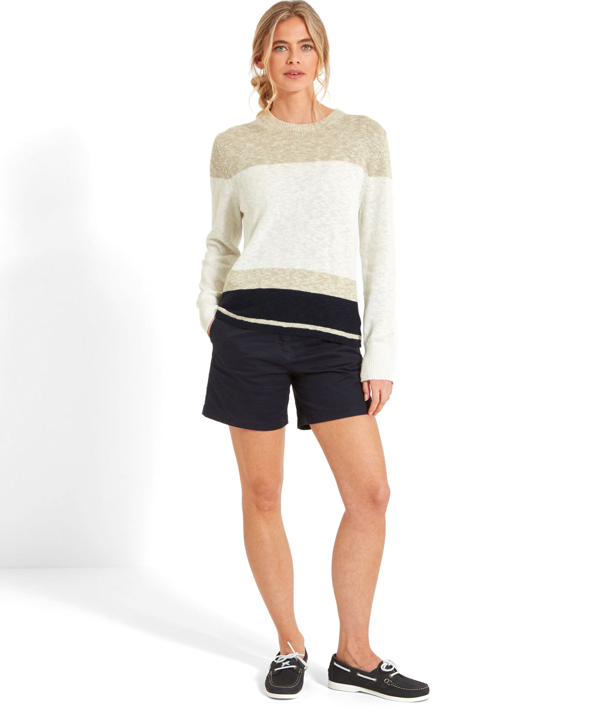 Full-body view of a woman wearing a Schöffel Treyarnon Bay Jumper for Women in Light Brown paired with navy shorts and black boat shoes.