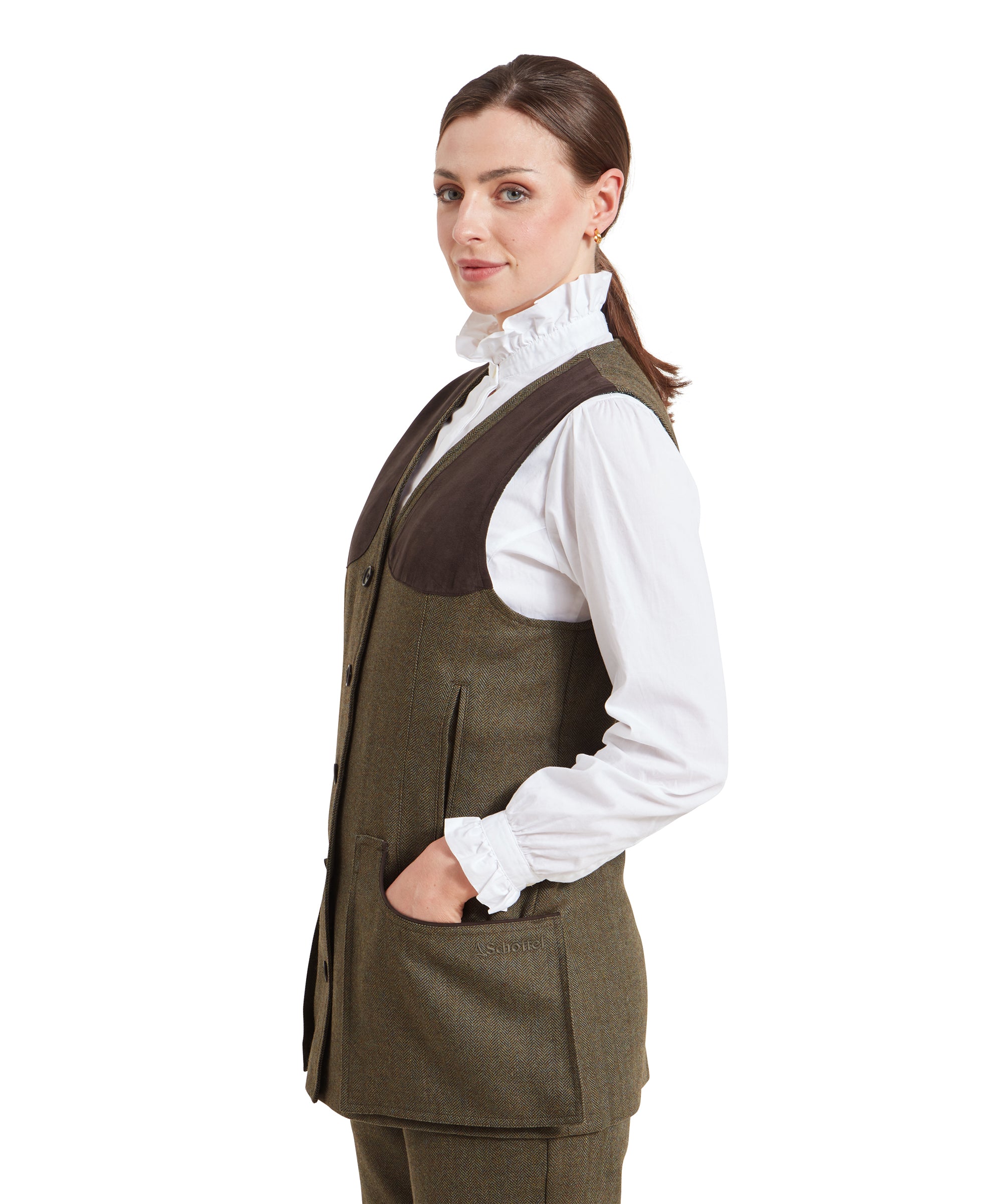 A side profile of the woman wearing the Schöffel Women's Tweed Shooting Vest for Womens in Green. The brown shoulder patch is clearly visible, and she has her hand in one of the large front pockets. The image emphasizes the tailored fit of the vest and the texture of the tweed fabric.