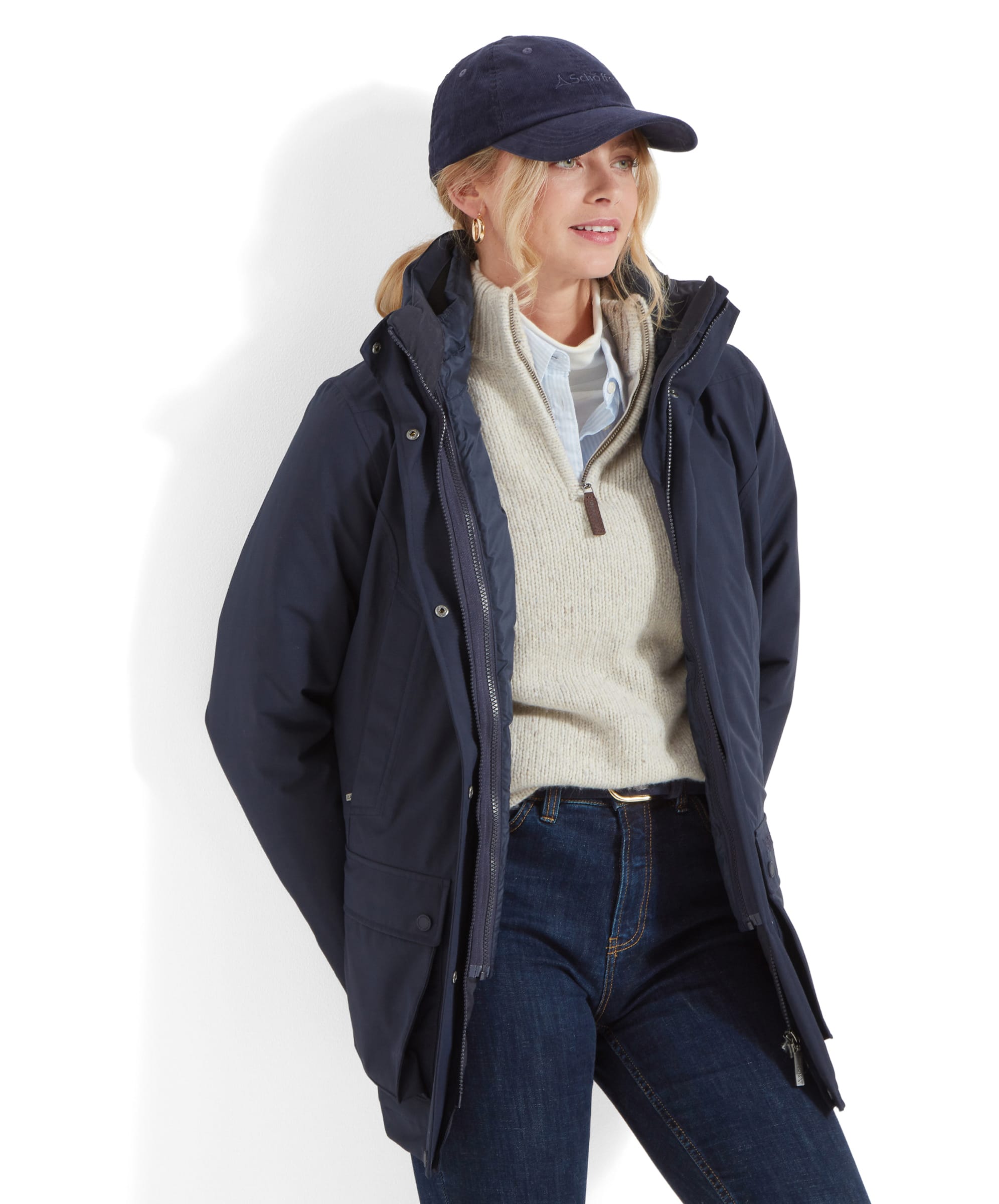 A rear view of the woman wearing the lightweight quilted insert from the Schöffel Uppingham 3-in-1 Coat for Women in Blue. Her blonde hair is tied back in a low ponytail, and she wears the same navy-blue baseball cap. The jacket’s horizontal quilting is visible, emphasising the jacket’s warmth and structure.