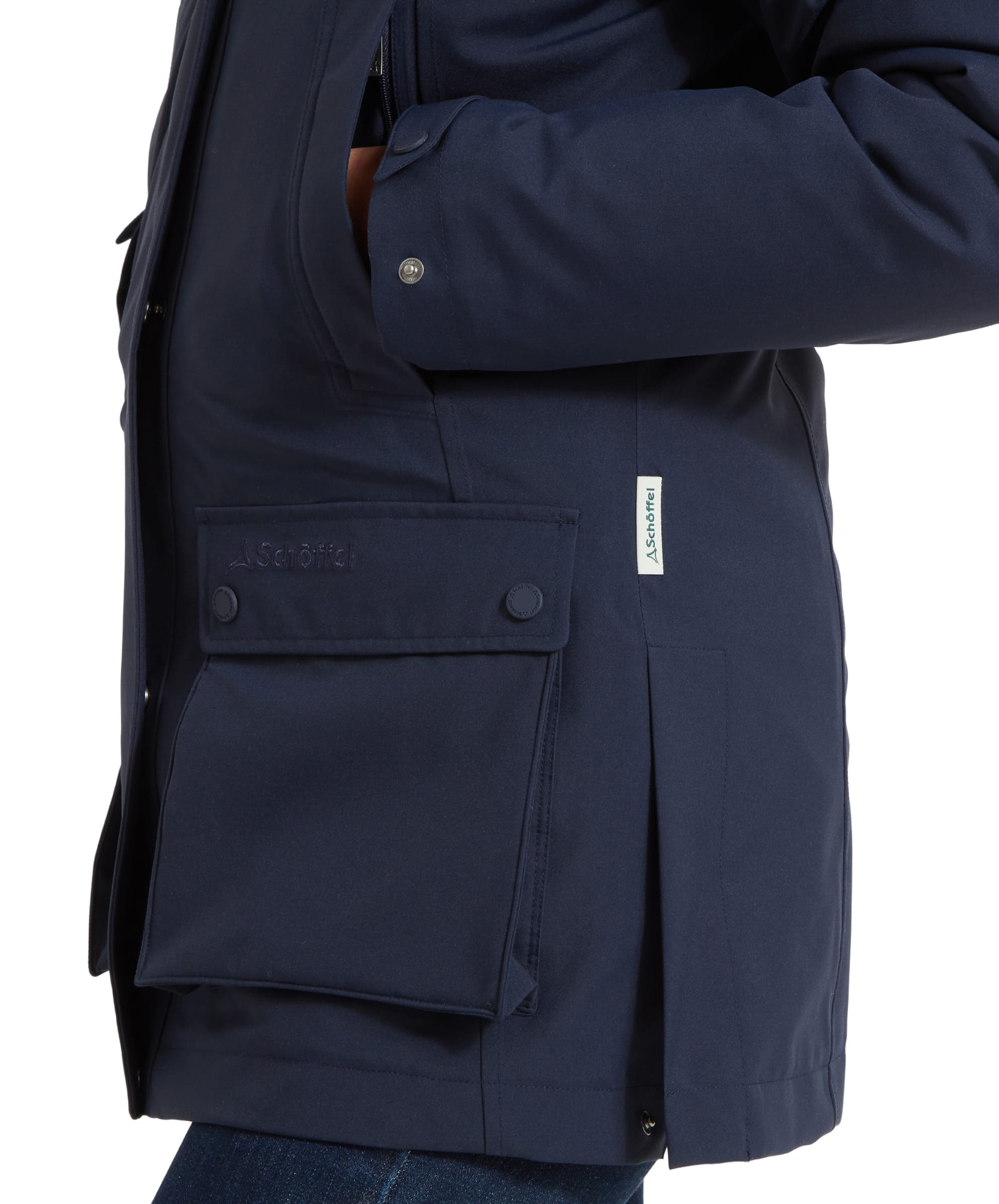 A close-up shot of the Schöffel Uppingham 3-in-1 Coat for Women in Blue’s lower front section, focusing on the coat’s pocket and the branding. The coat features a flap pocket with a button closure and visible stitching details, along with a small Schöffel label on the side.