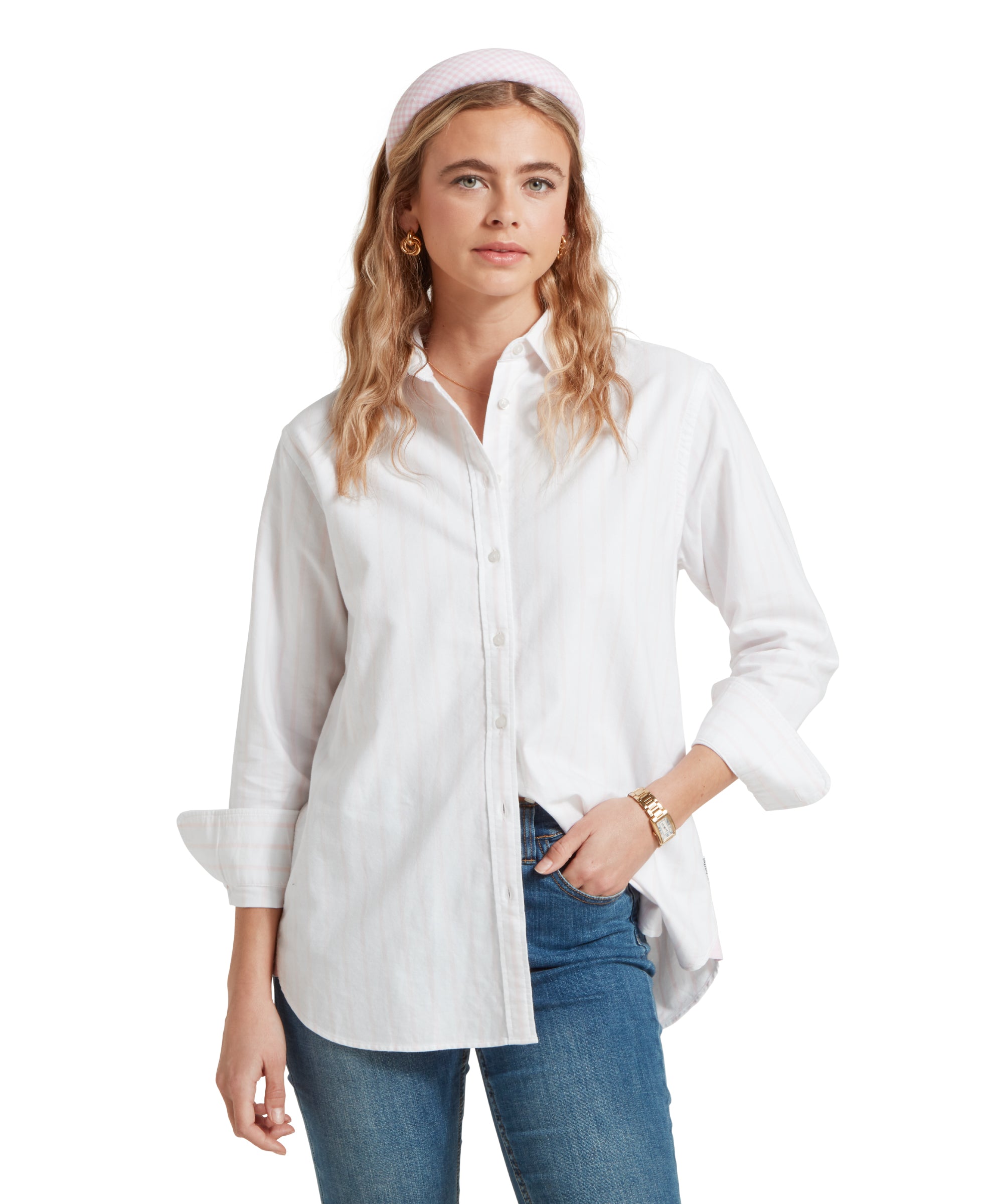 Close-up of a female model wearing a white and pink striped Schöffel shirt, paired with a pair of mid wash denim jeans. She is standing in a relaxed pose with one hand in her pocket.