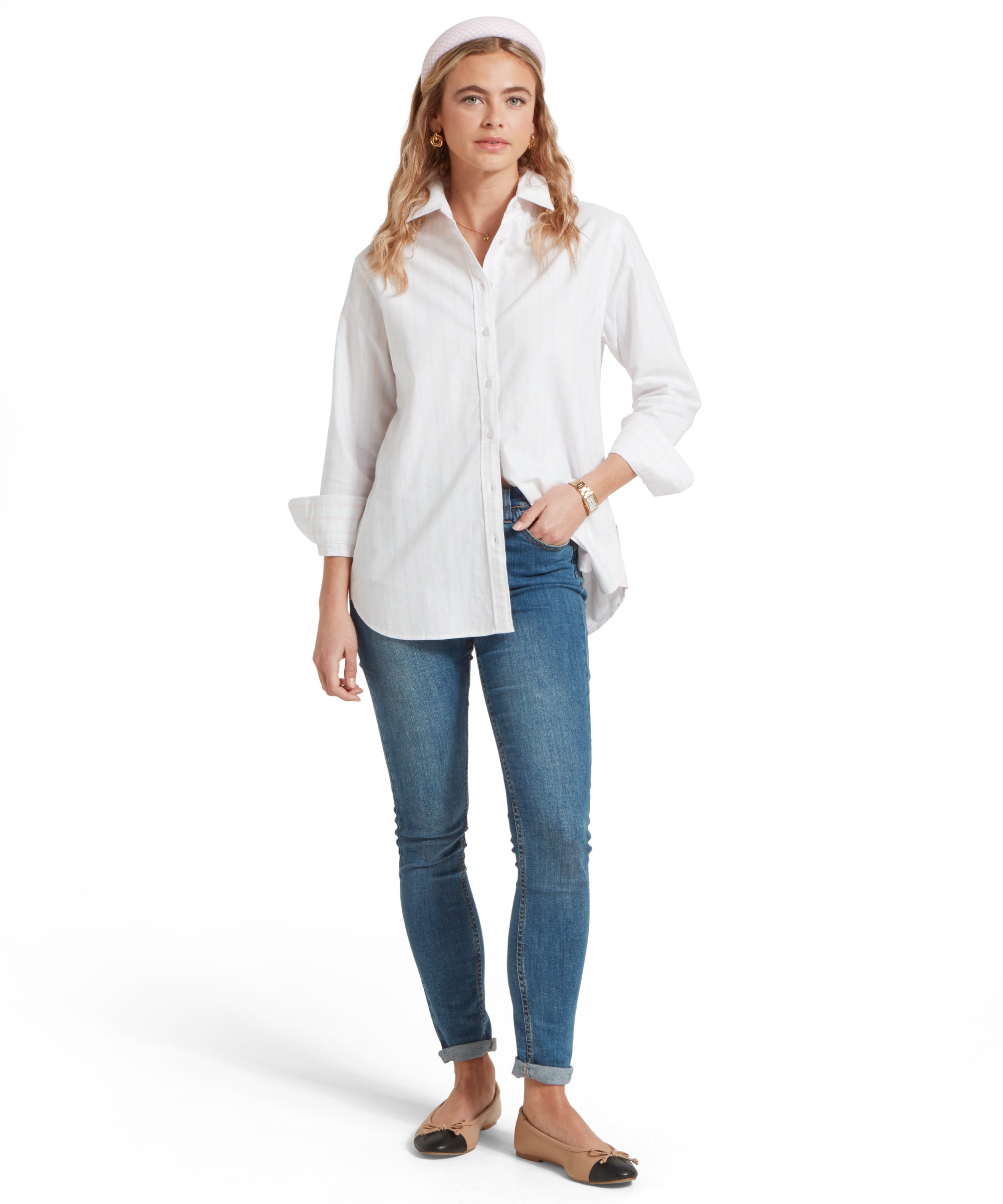 Full height image of a female model wearing a white and pink striped Schöffel shirt, paired with a pair of mid wash denim jeans and tan pumps. She is standing in a relaxed pose with one hand in her pocket.