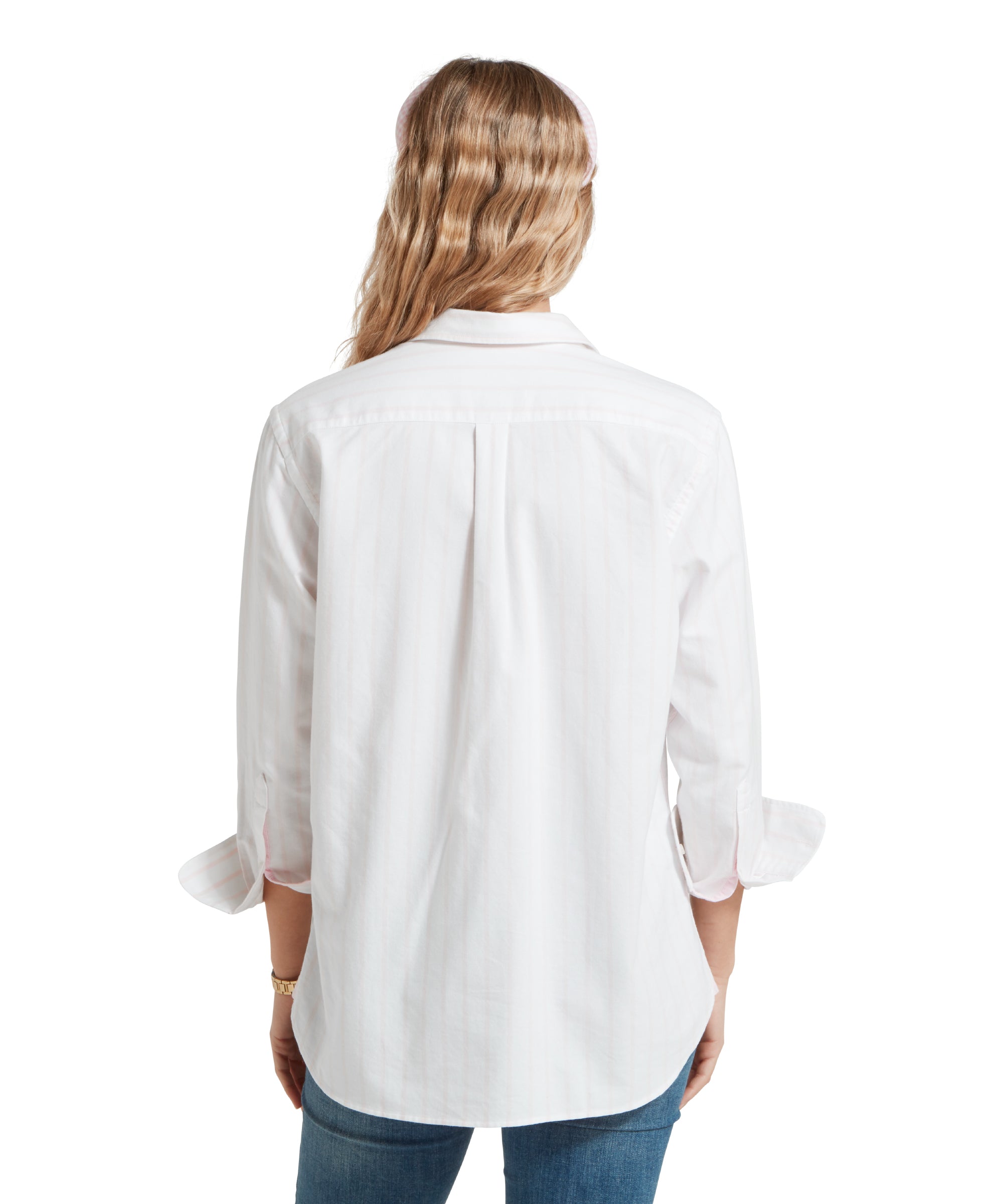 Back image of a female model wearing a white and pink striped Schöffel shirt, paired with a pair of mid wash denim jeans. She is standing in a relaxed pose with her hands to her side.