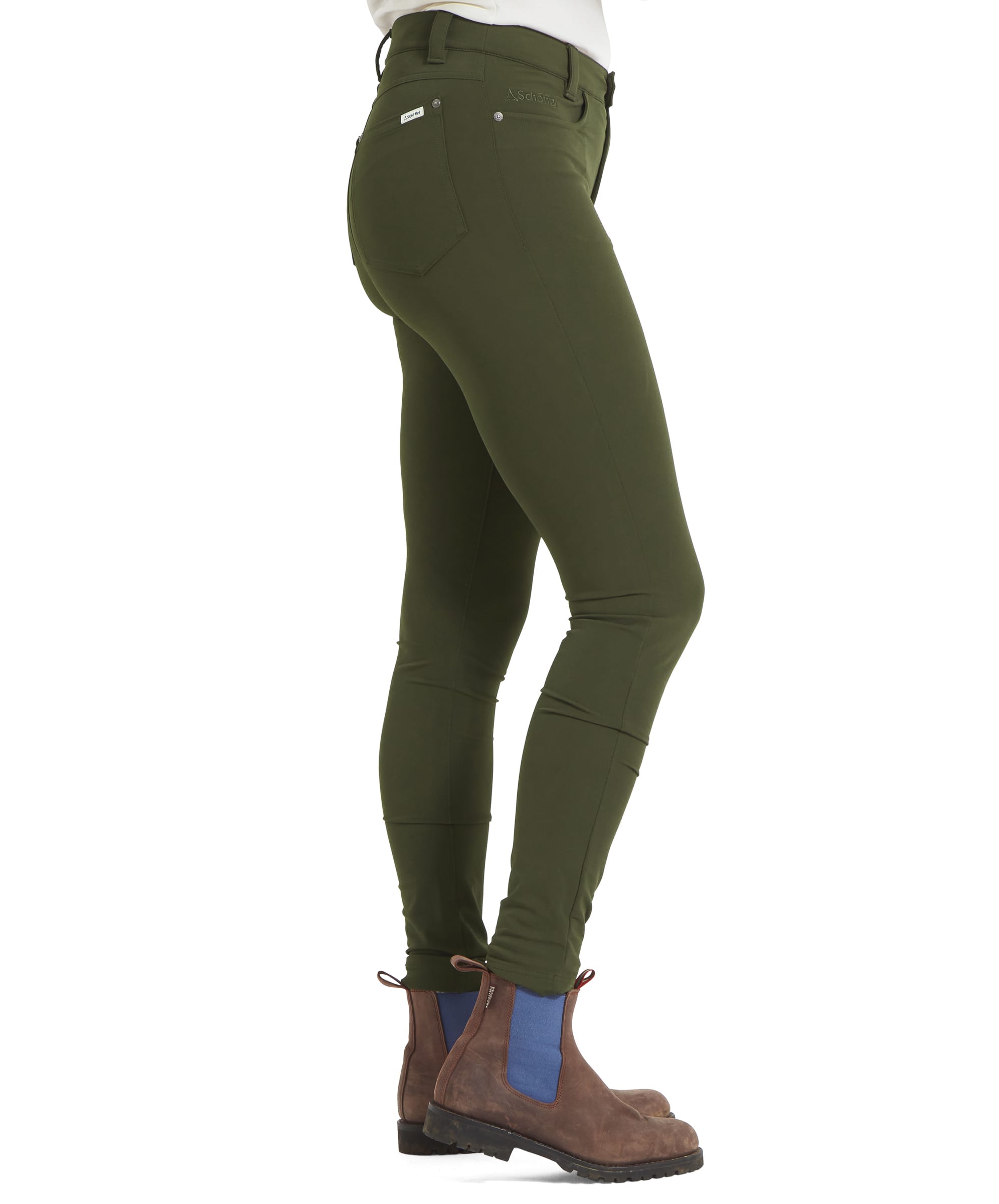 This side profile image showcases the fit of the Schöffel Whitwell Water Repellent Trouser for Women in Green on the model's leg, from hip to ankle. The trousers have a slim and snug fit, accentuating the leg shape. The model’s brown boots with blue elastic panels are visible from the side, complementing the trousers.