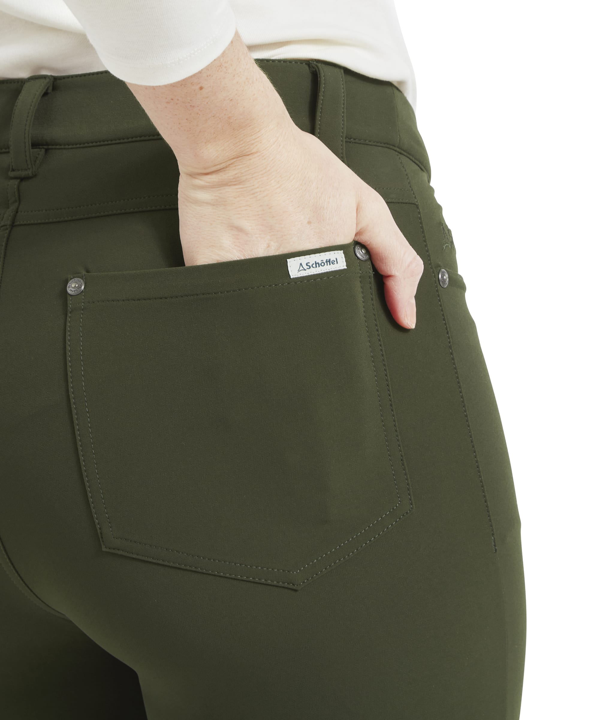 The image focuses on the back pocket of the Schöffel Whitwell Water Repellent Trouser for Women in Green, showing the pocket's stitching and the small brand label sewn onto the pocket. The model’s hand is partially placed inside the pocket, highlighting its size and positioning.