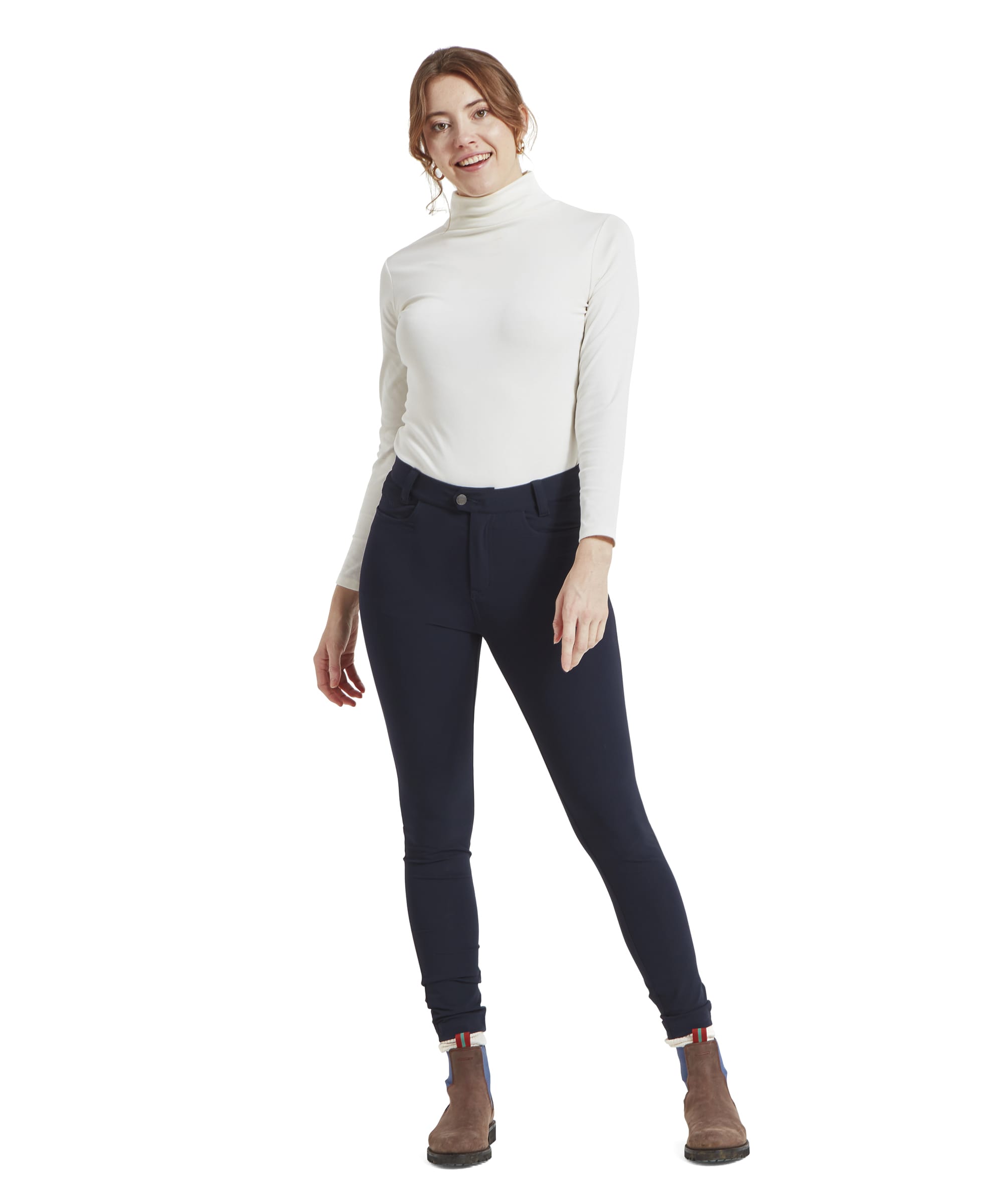 Full-body view of a model wearing the Schöffel Whitwell Water Repellent Trouser for Women in Blue as she smiles kindly toward the camera. The trousers are partnered with a cream turtleneck long sleeve top and brown suede boots.