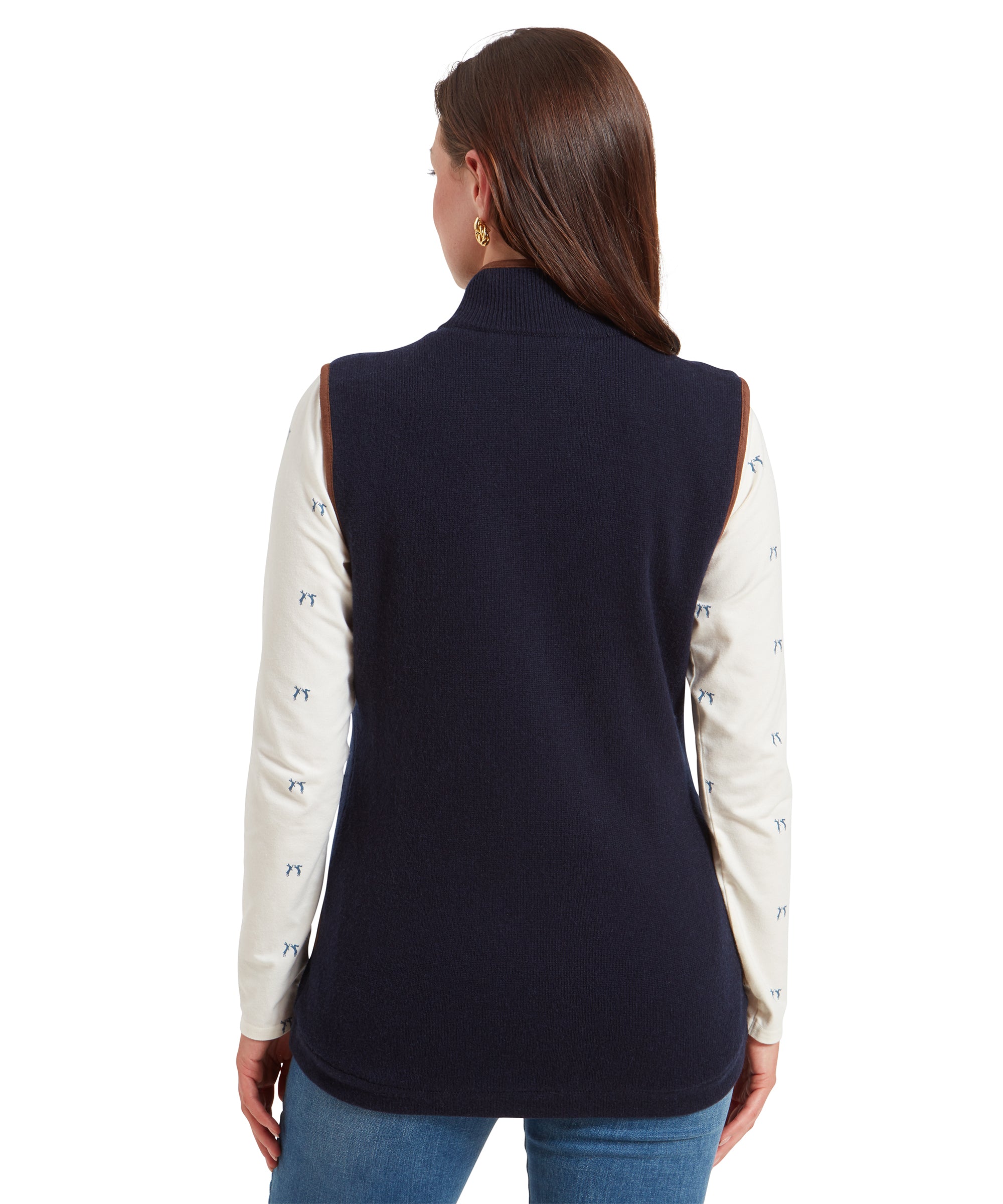 A back view of a woman wearing a Schöffel Women's Lambswool Aerobloc Gilet for Womens in Navy with brown trim, showing the garment's length and fit. The cream top underneath features a subtle print.