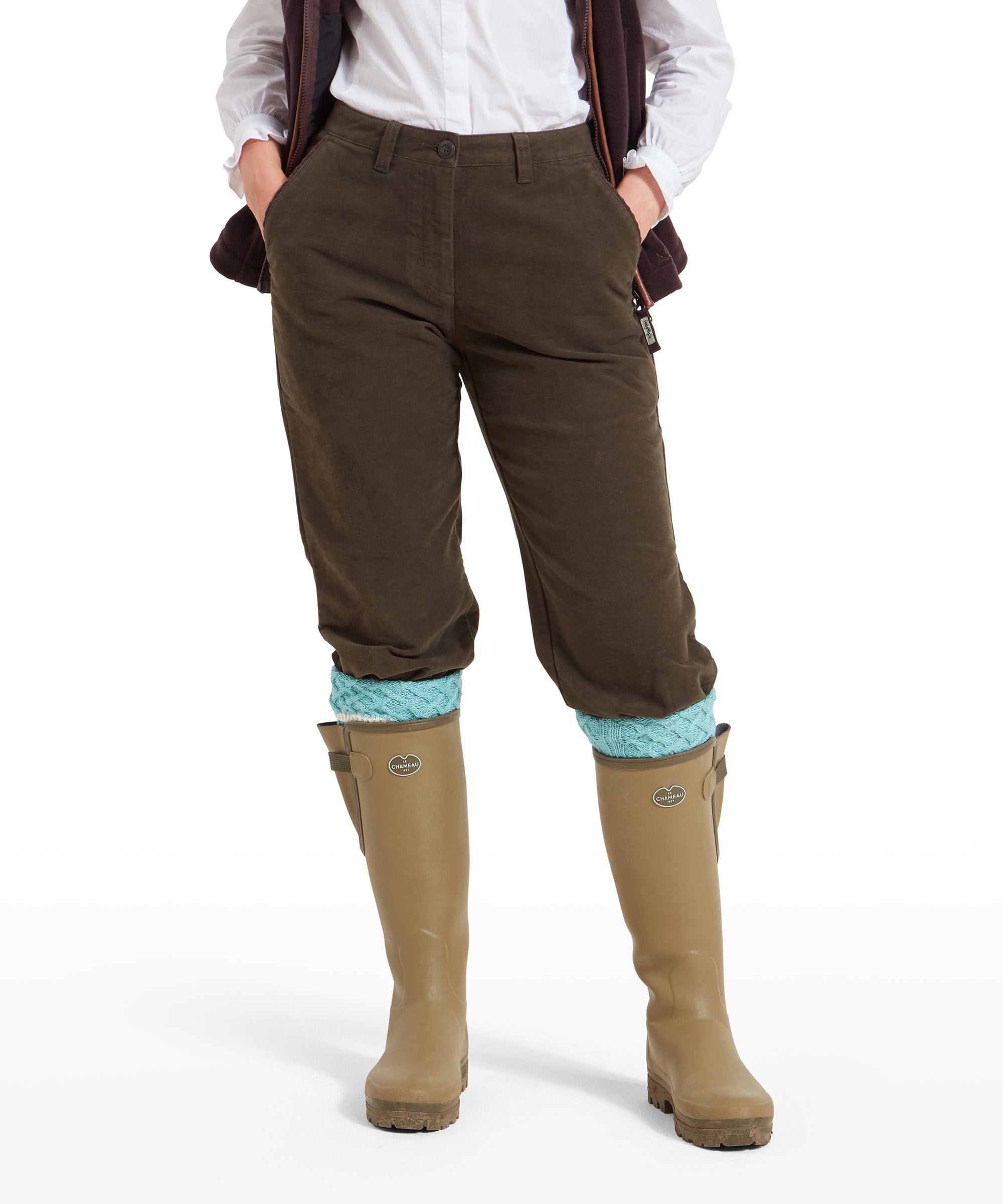 A close-up view of a woman wearing Schöffel Moleskin Breeks for Womens in Green with a white shirt. The breeks are tucked into beige wellington boots with light blue knit socks peeking out at the top. The hands are in the pockets, highlighting the fit and texture of the breeks.